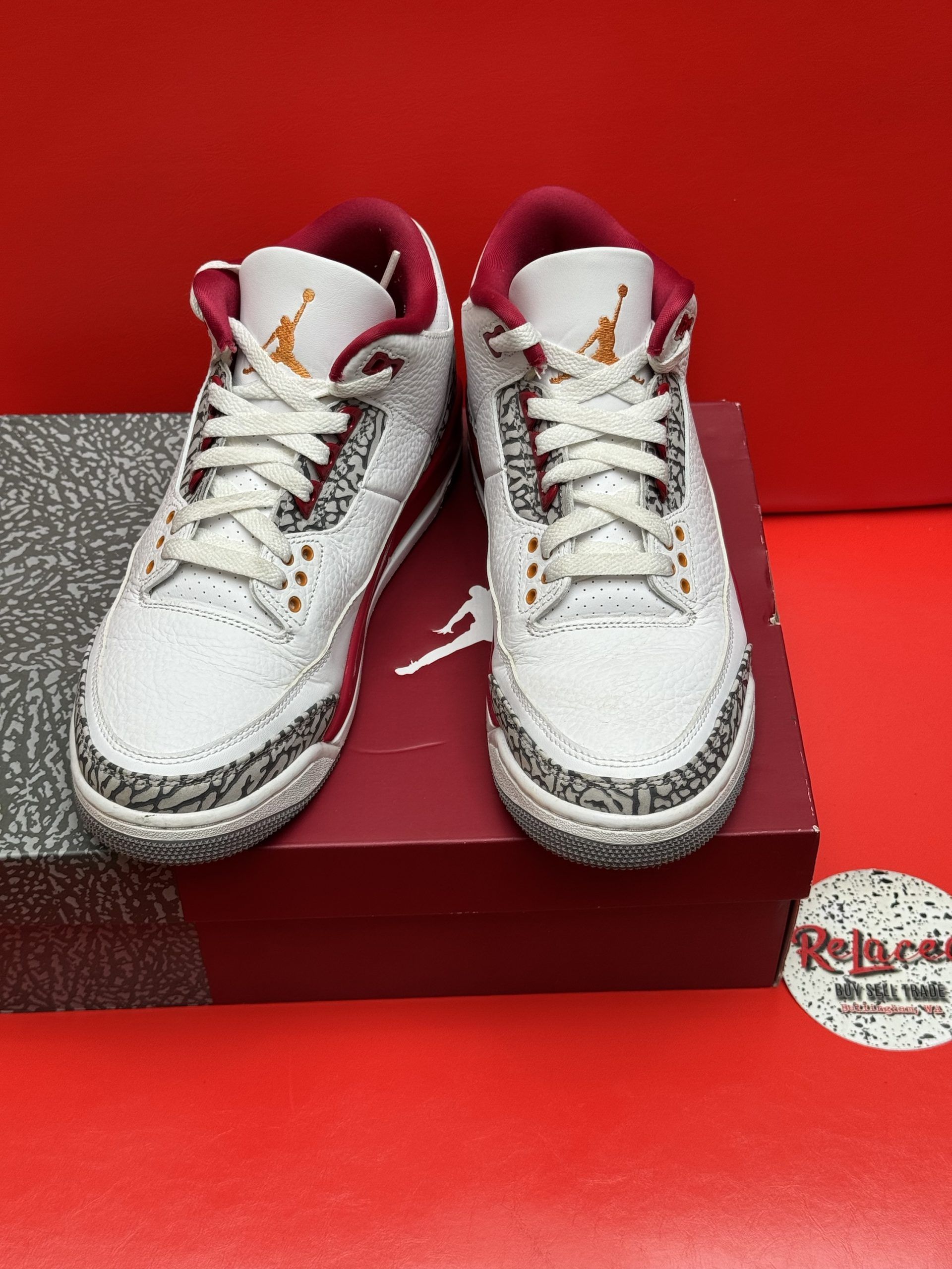 Air Jordan 3 sneakers in white, red, and grey, on a red shoebox, set against a red background.