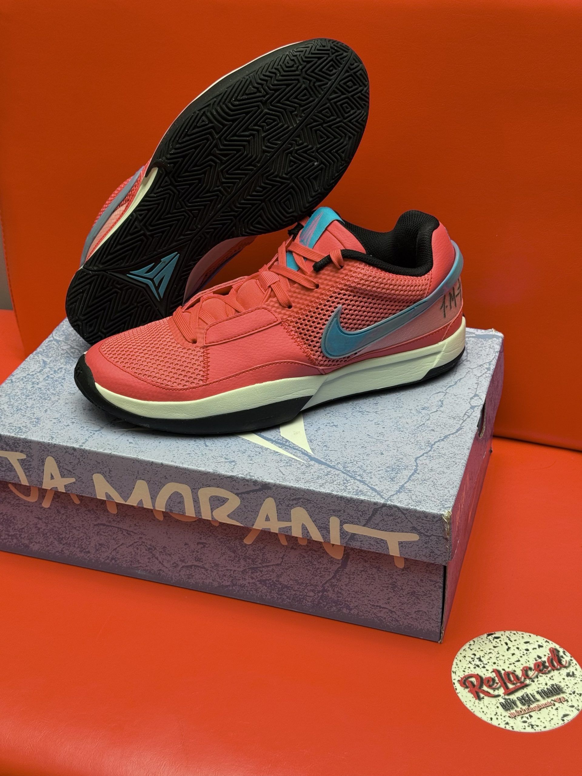Red and blue Nike Ja Morant sneakers on a purple box, one shoe up, resting on a red surface.