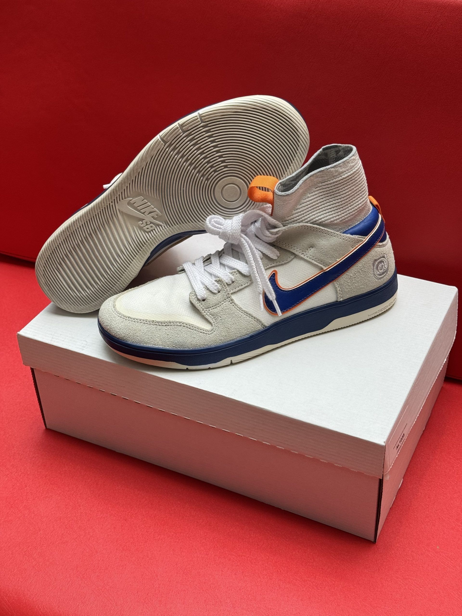 White and blue sneakers on a white box against a red background. One shoe sole visible.