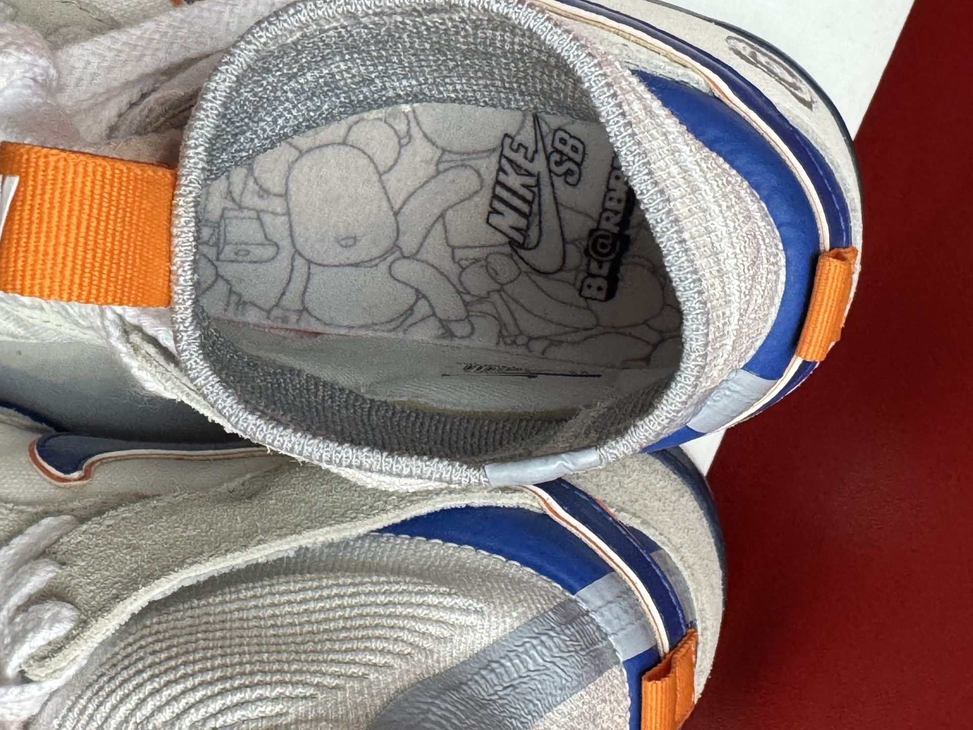 White and blue sneakers on a white box against a red background. One shoe sole visible.