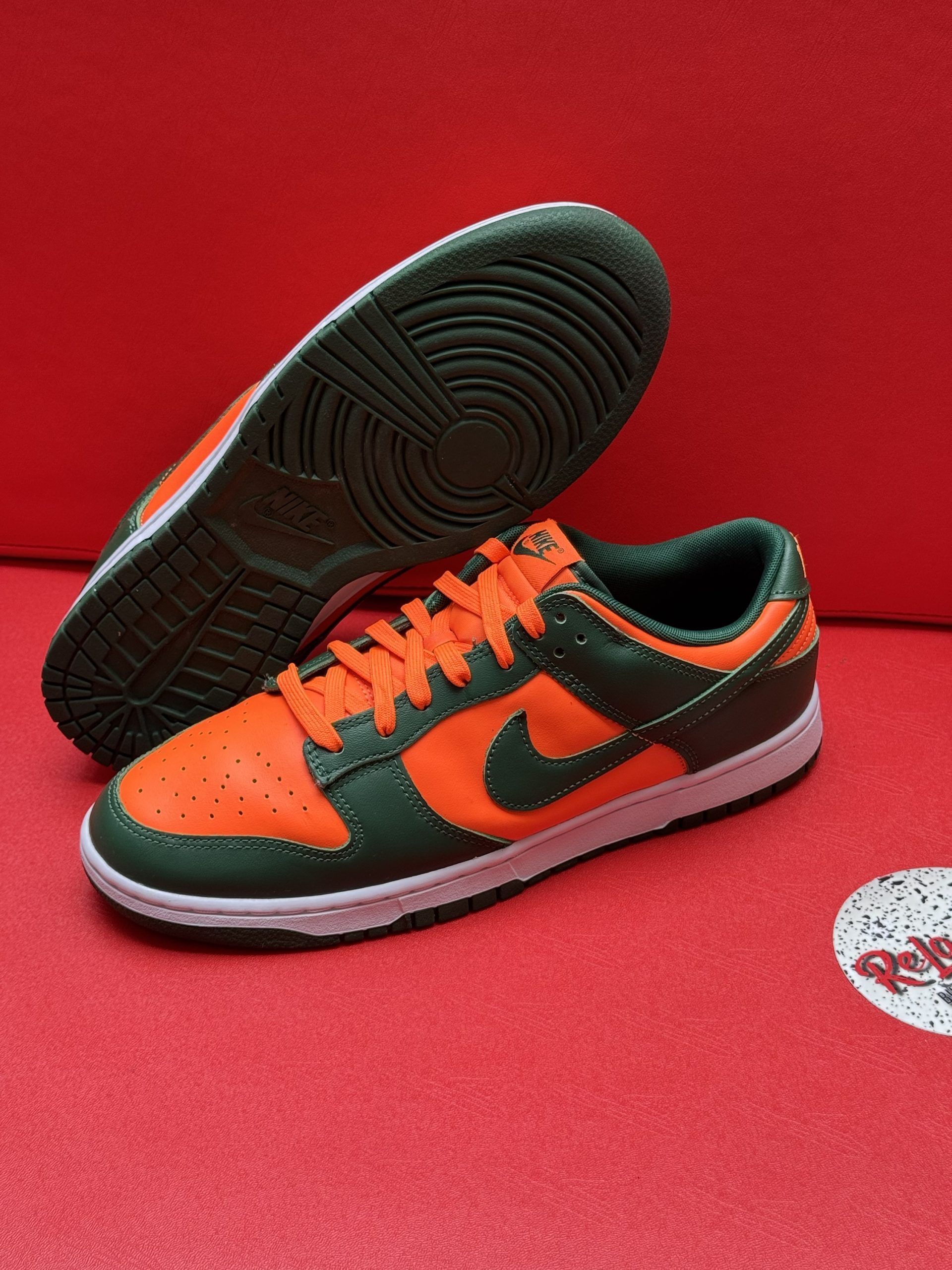 Orange and green Nike Dunk Low sneakers with white soles, on a red surface.