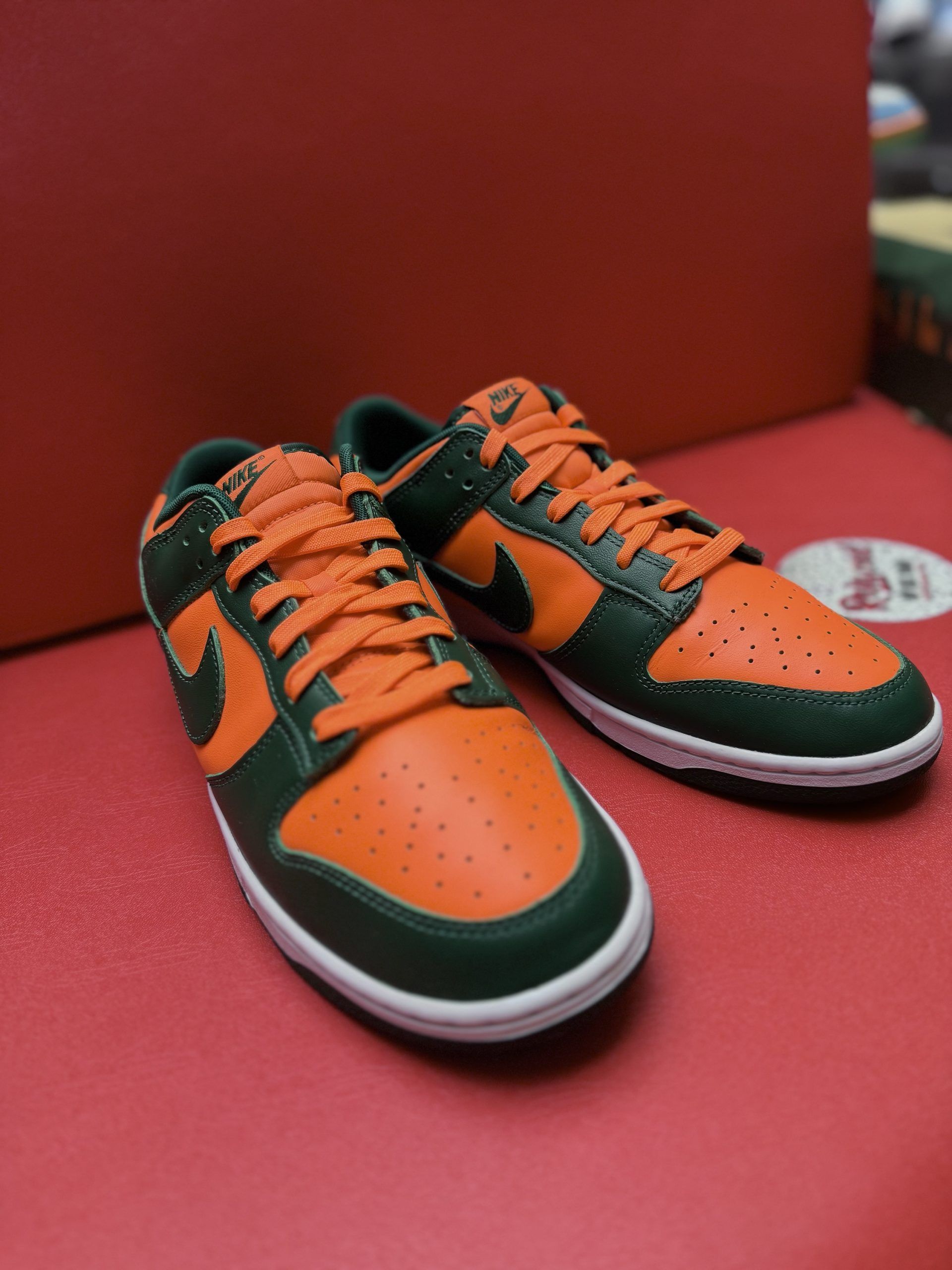 Orange and green Nike Dunk Low sneakers with white soles, on a red surface.
