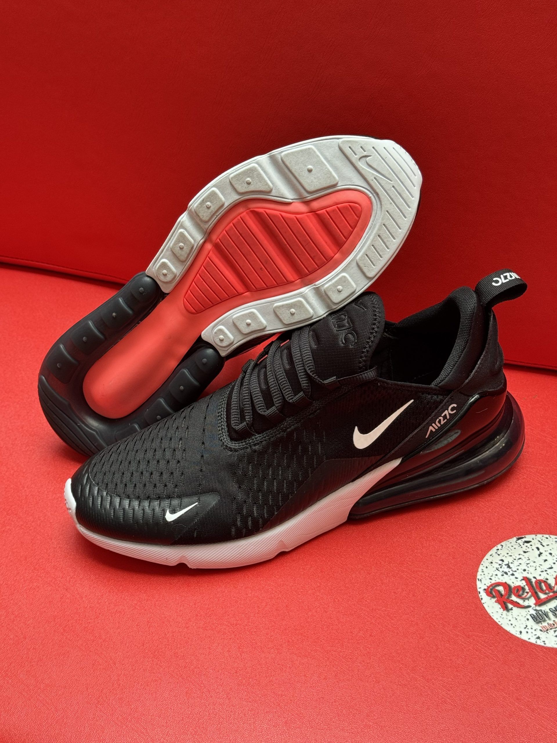 Black Nike Air Max 270 sneakers with white swooshes and a red sole, set against a red backdrop.