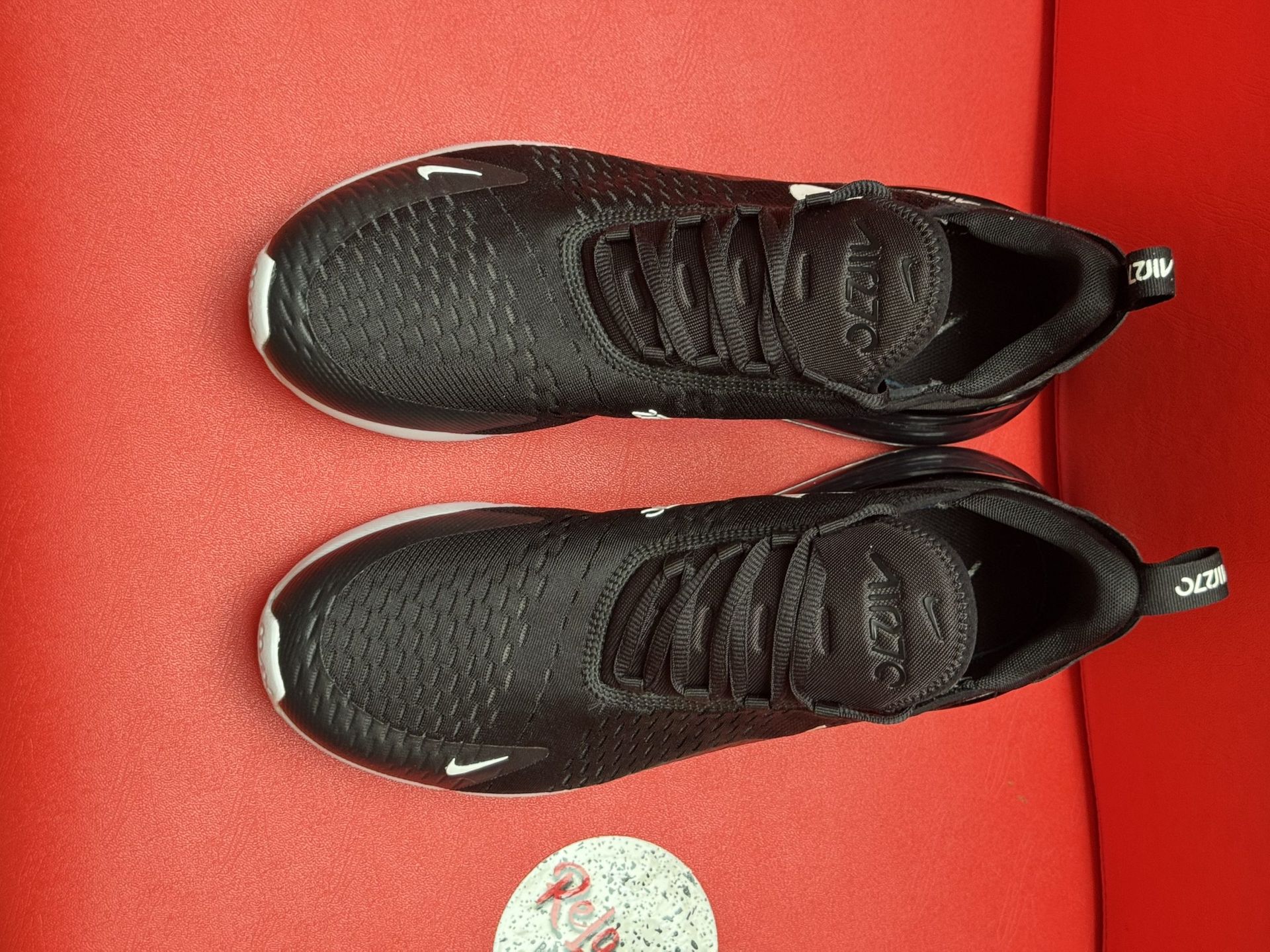 Black Nike Air Max 270 sneakers with white swooshes and a red sole, set against a red backdrop.