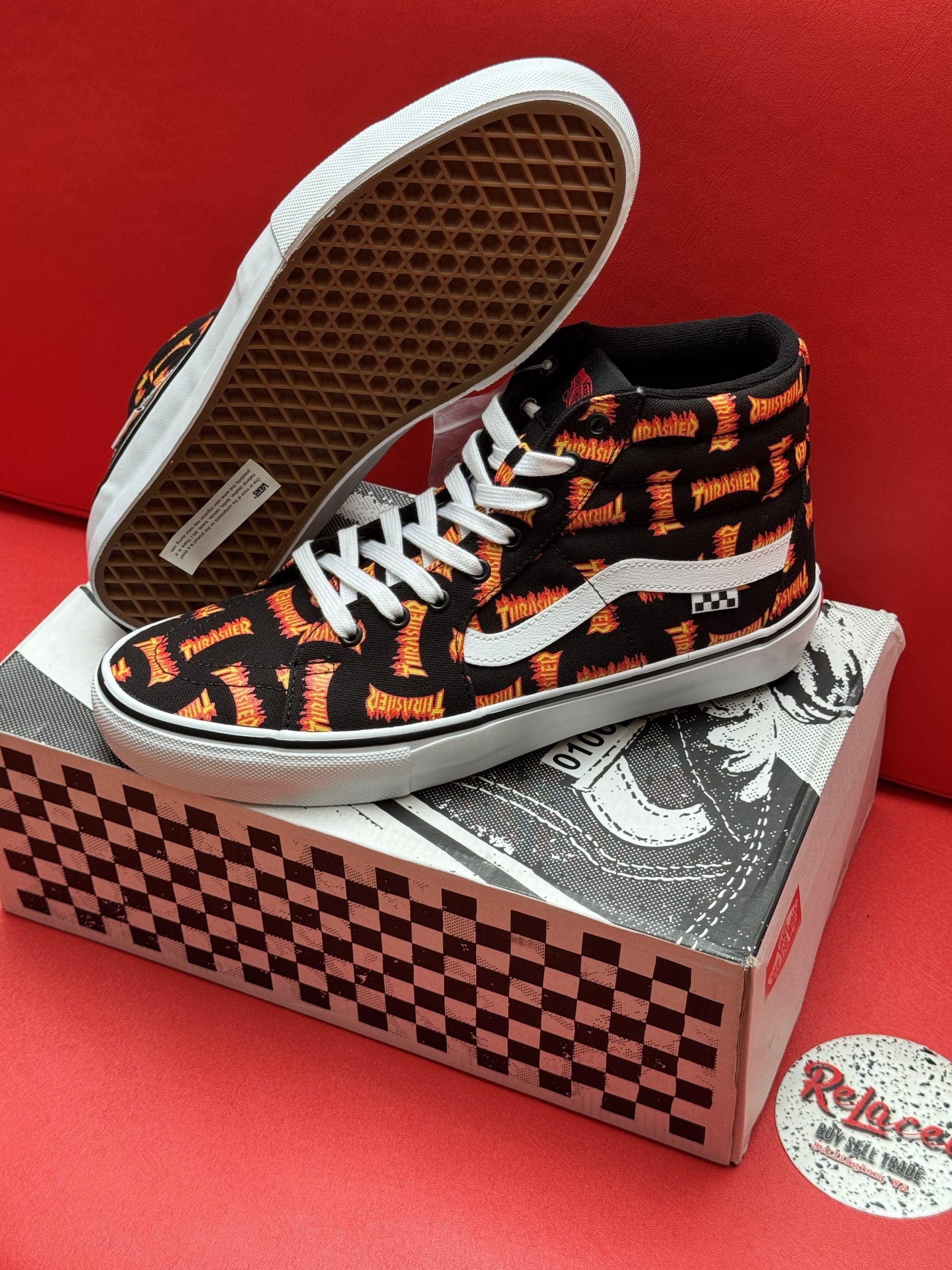 Pair of Vans high-top sneakers with a black and orange pattern, white soles, and a black box with a checkerboard pattern.