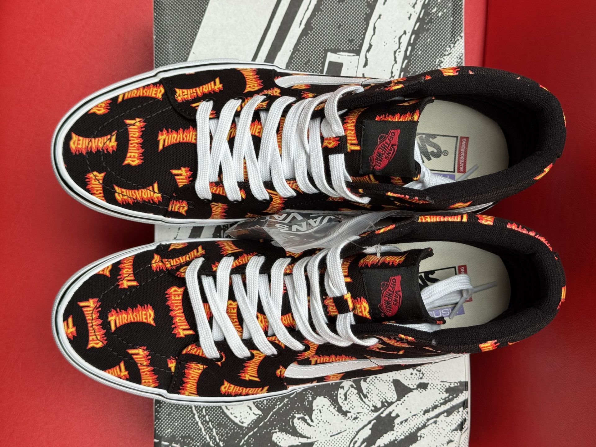 Pair of Vans high-top sneakers with a black and orange pattern, white soles, and a black box with a checkerboard pattern.