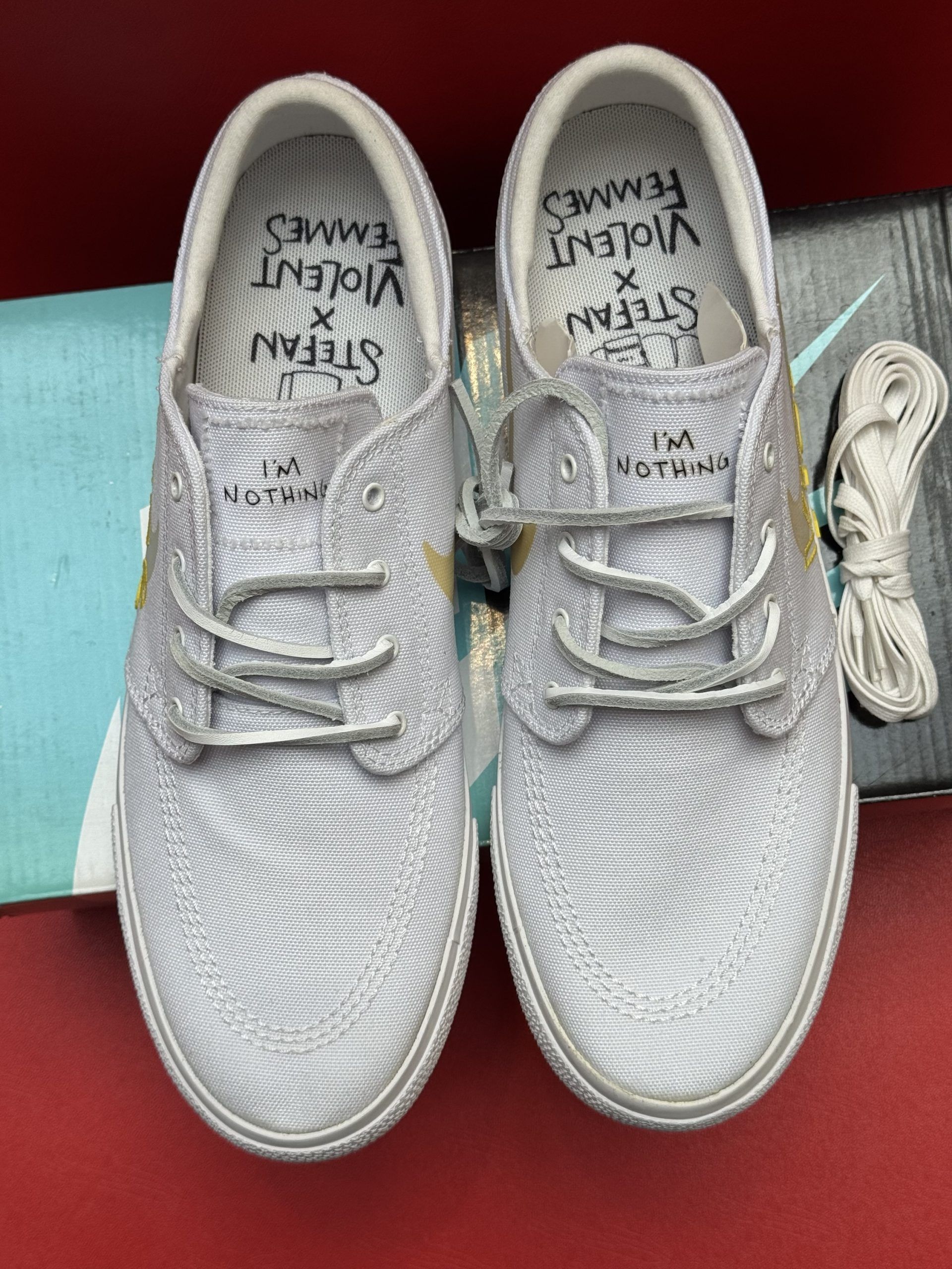 White Nike SB Janoski sneakers with a yellow Swoosh, atop a shoe box.