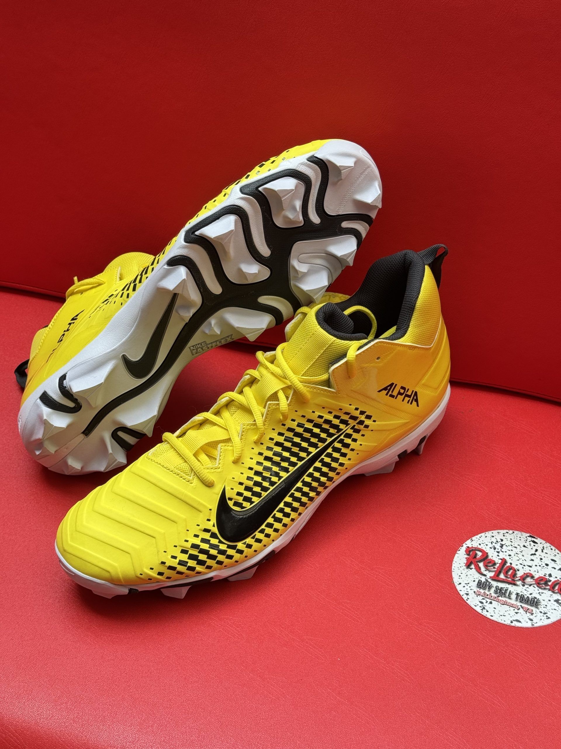 Yellow Nike Alpha football cleats on a red surface. Black Nike swoosh, white and black sole.
