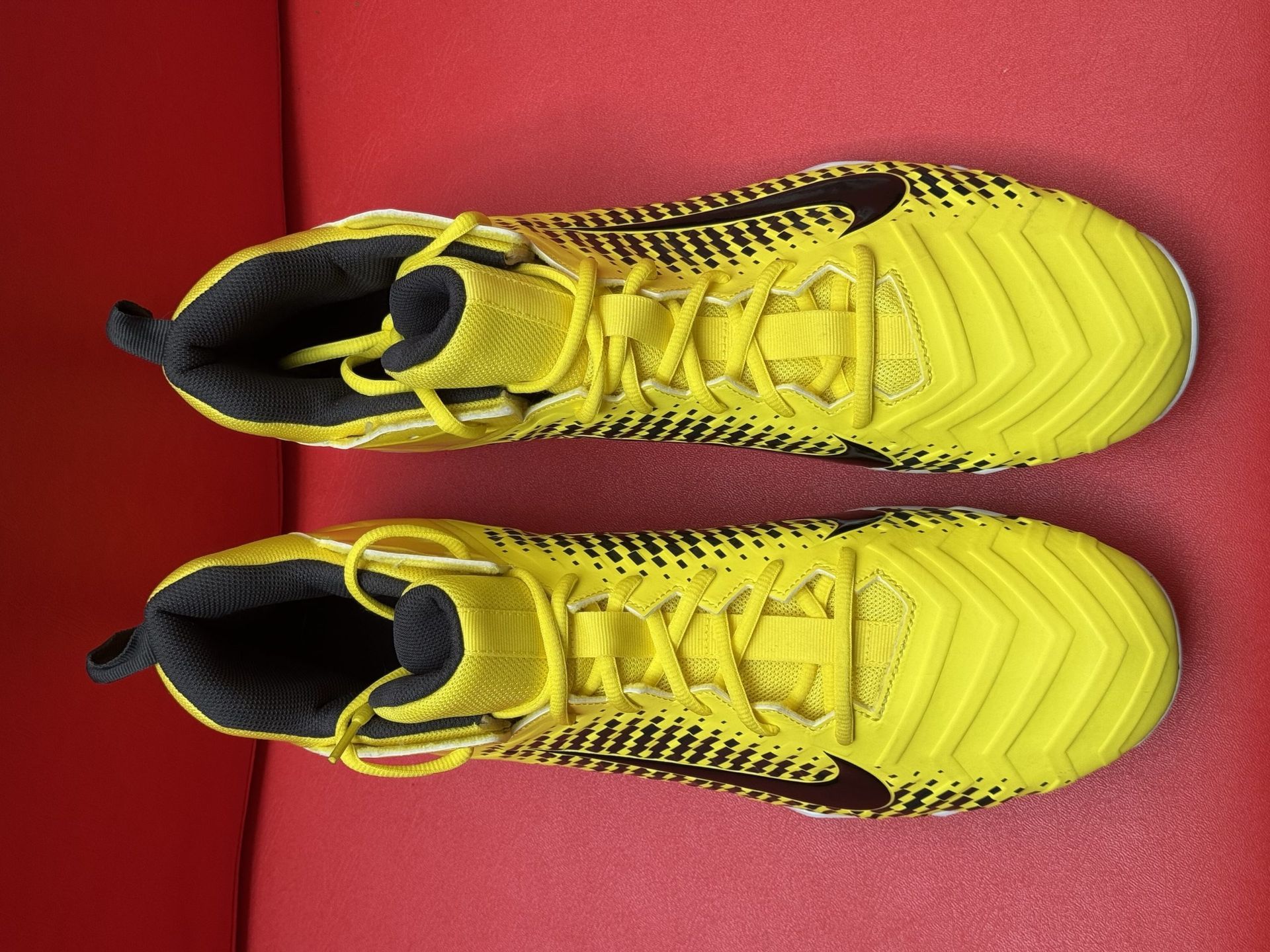 Yellow Nike Alpha football cleats on a red surface. Black Nike swoosh, white and black sole.