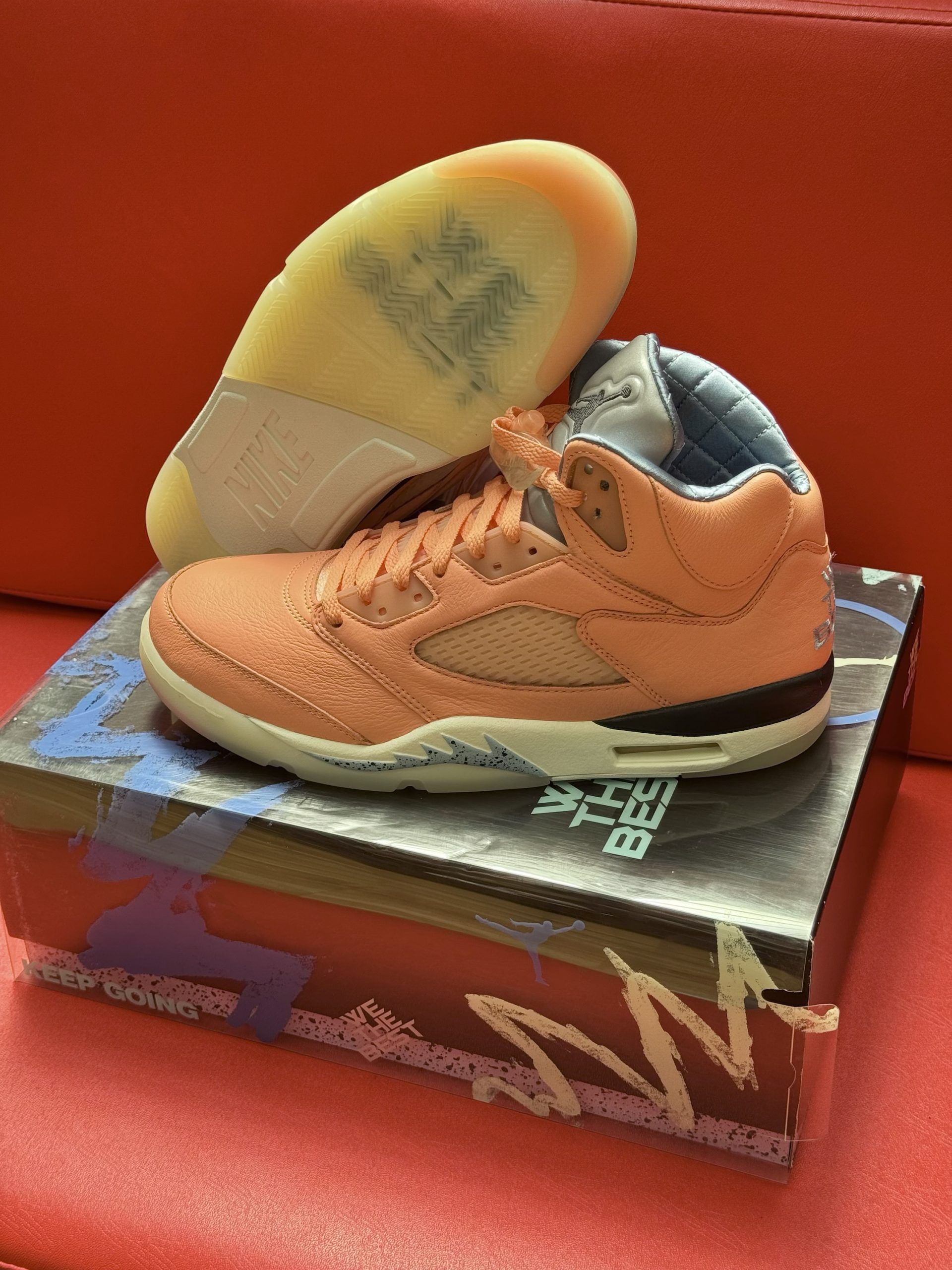 Peach-colored Air Jordan 5 sneakers with a translucent sole, resting on a box against a red background.
