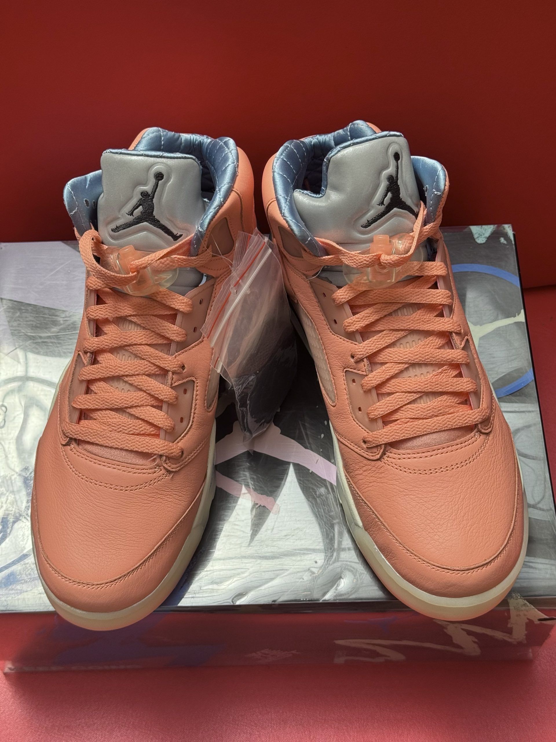 Peach-colored Air Jordan 5 sneakers with a translucent sole, resting on a box against a red background.