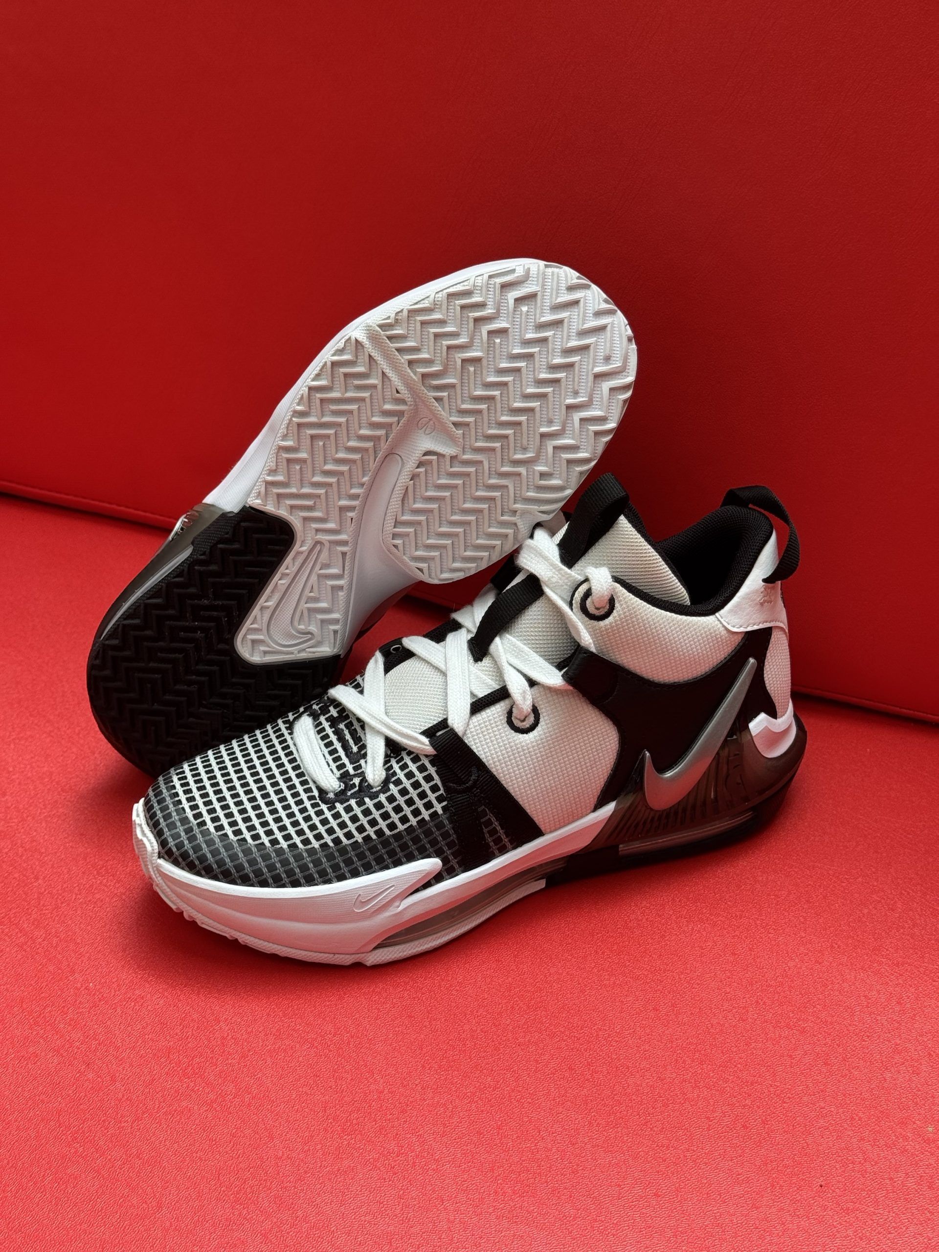 White and black Nike basketball shoe pair on a red surface.