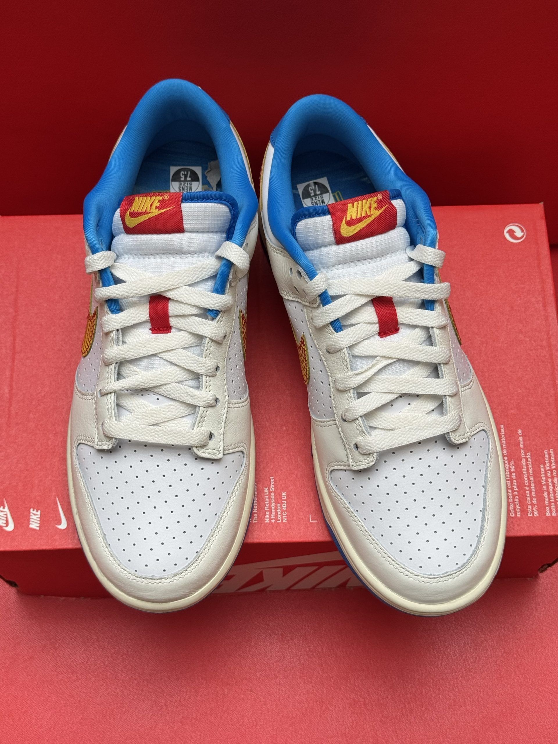 White Nike Dunk low sneakers with yellow and red accents on a red box, blue sole.