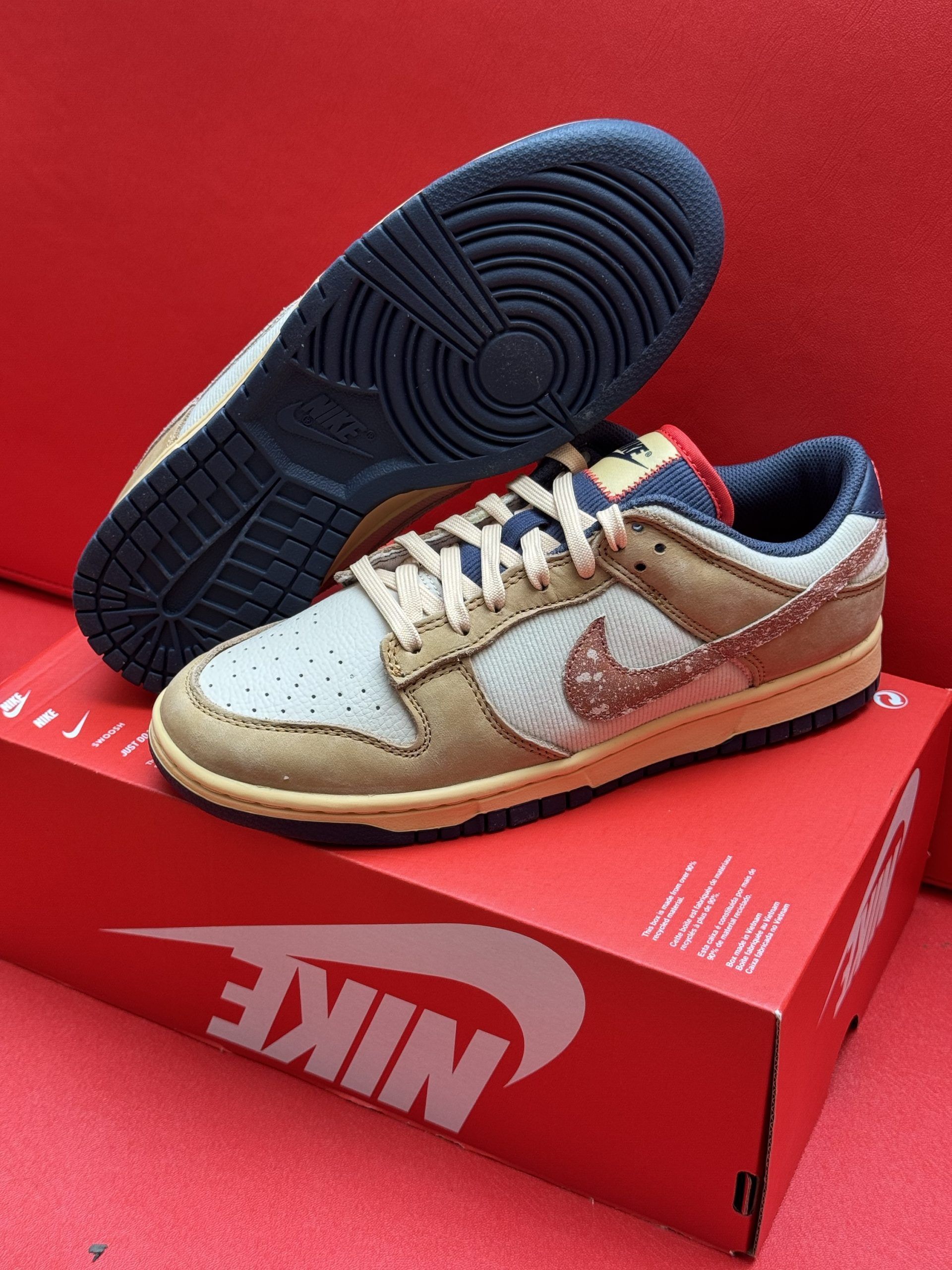 Nike Dunk Low sneakers in tan and blue on a red Nike box with a red background.