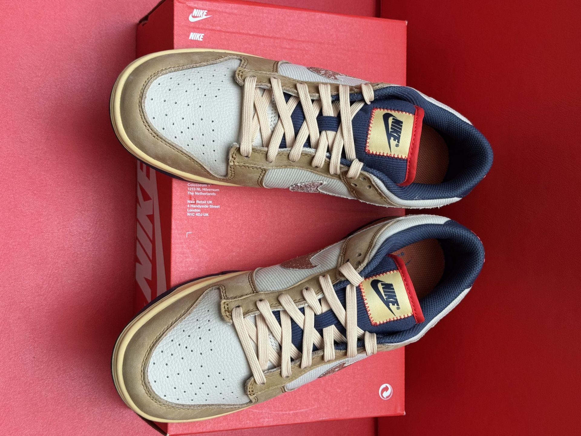Nike Dunk Low sneakers in tan and blue on a red Nike box with a red background.