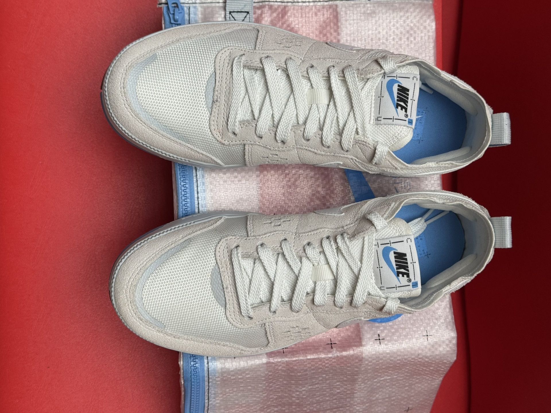 White Nike sneakers with a blue sole and logo, resting on a Nike box, set against a red background.