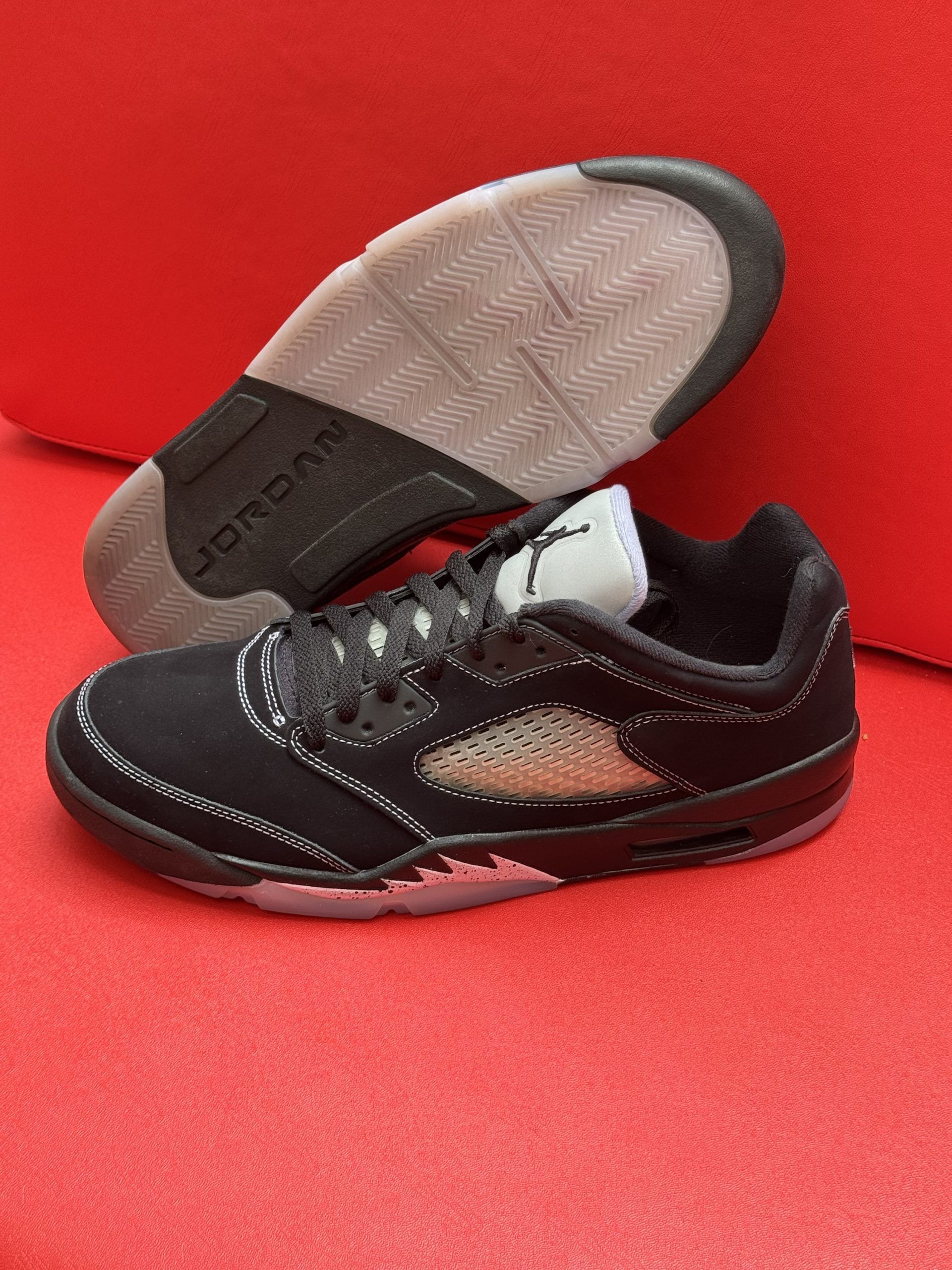 Black and gray Air Jordan 5 low-top sneaker on a red surface; sole visible.