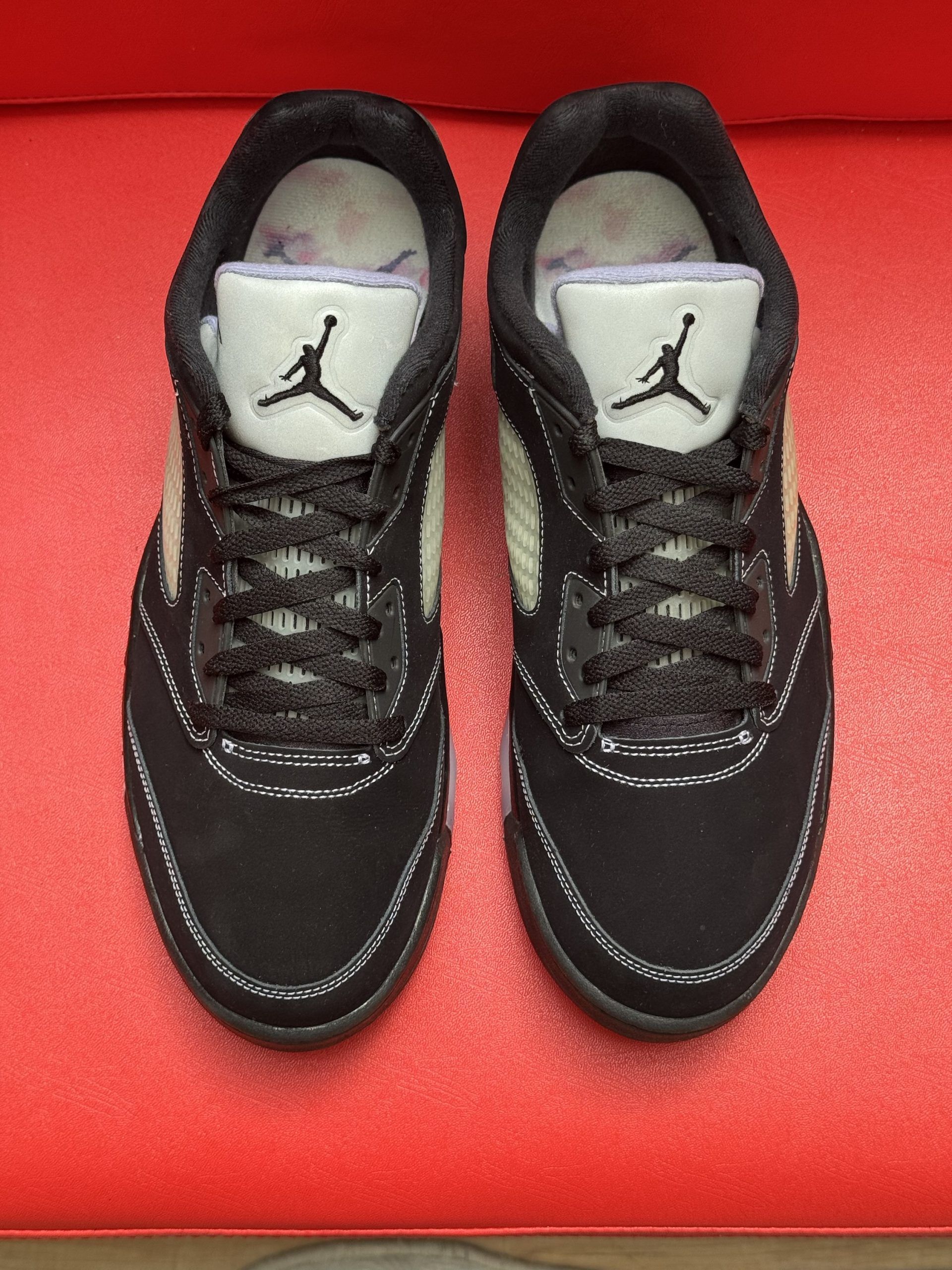 Black and gray Air Jordan 5 low-top sneaker on a red surface; sole visible.