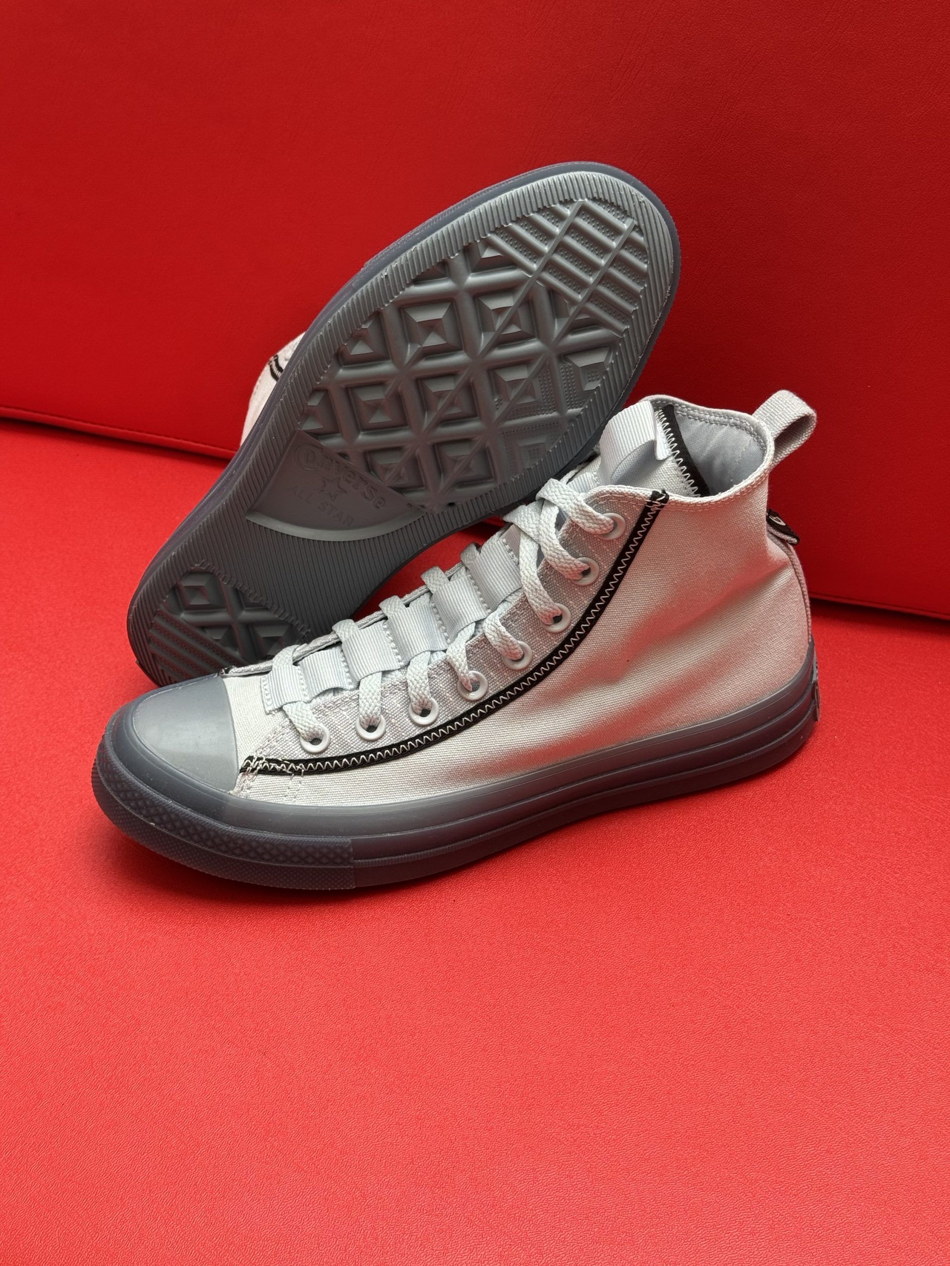 Gray high-top Converse sneakers with black trim on a red surface, sole visible.