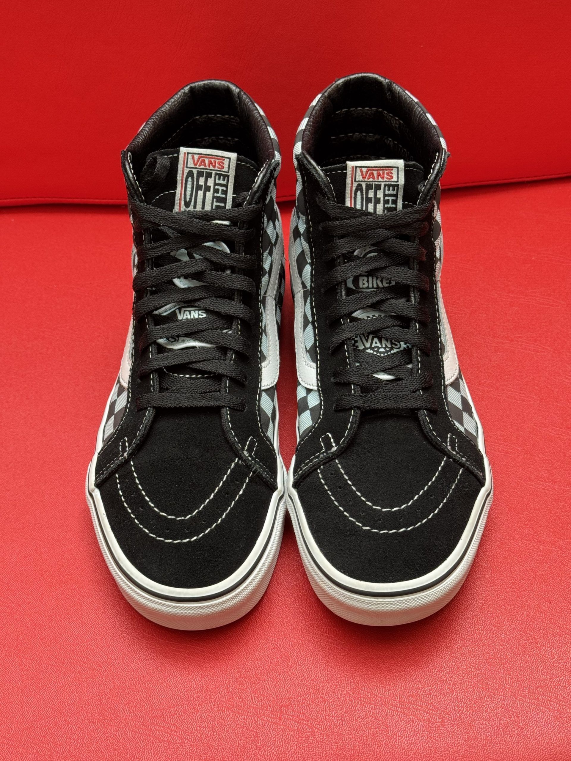 High-top Vans sneakers with black and white checkerboard pattern on a red surface.