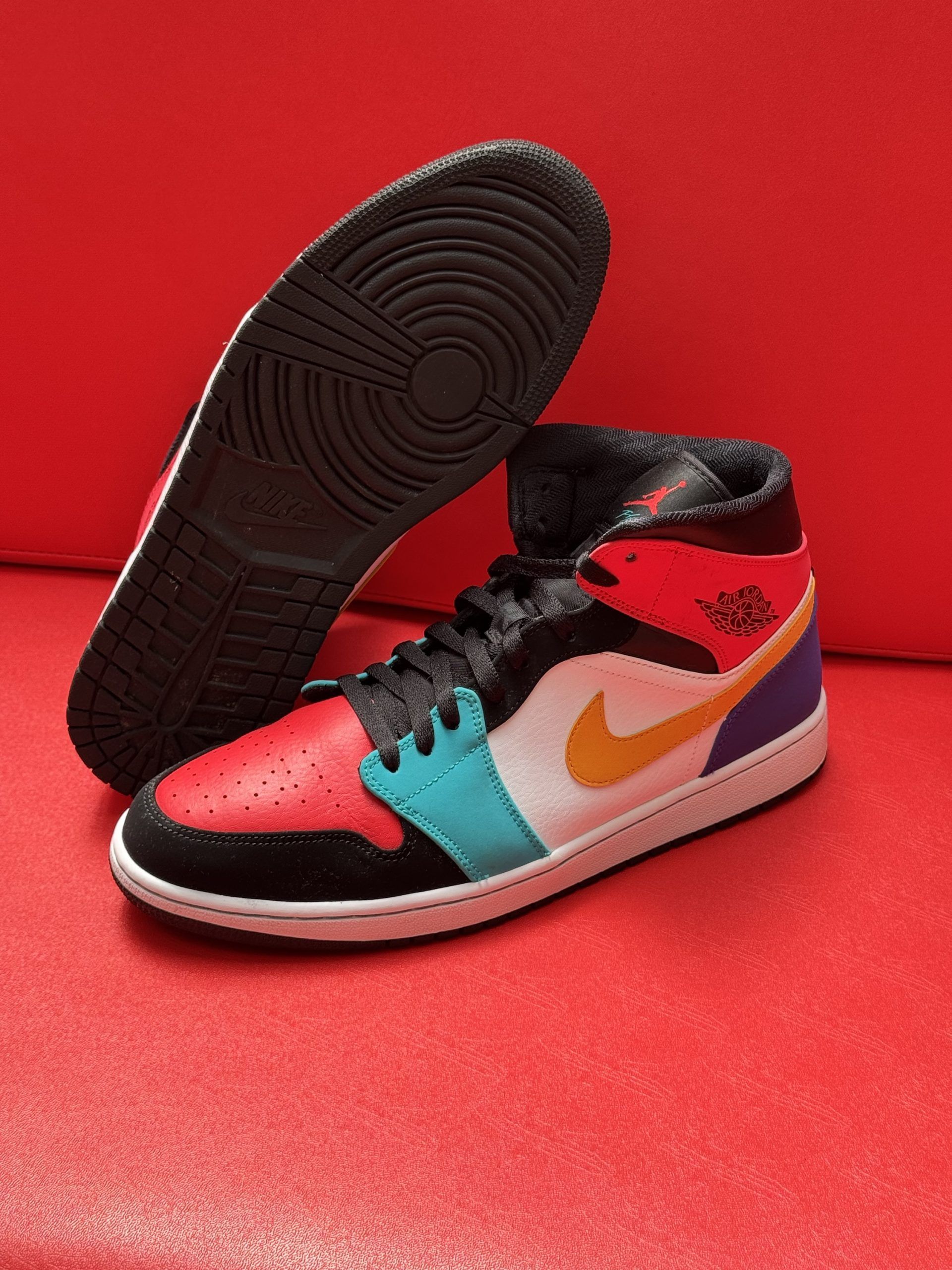 Colorful Air Jordan mid-top sneaker on a red surface, with the sole next to it.