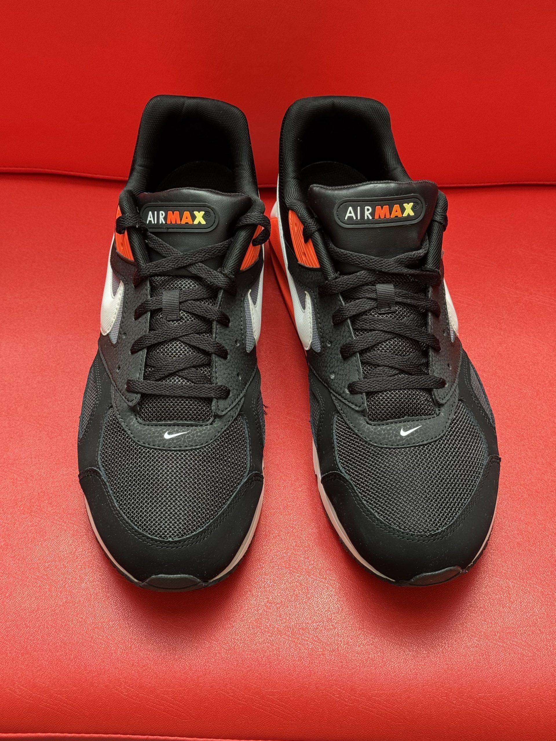 Black and orange Nike Air Max sneakers on a red surface. One shoe is upside down, revealing the sole.