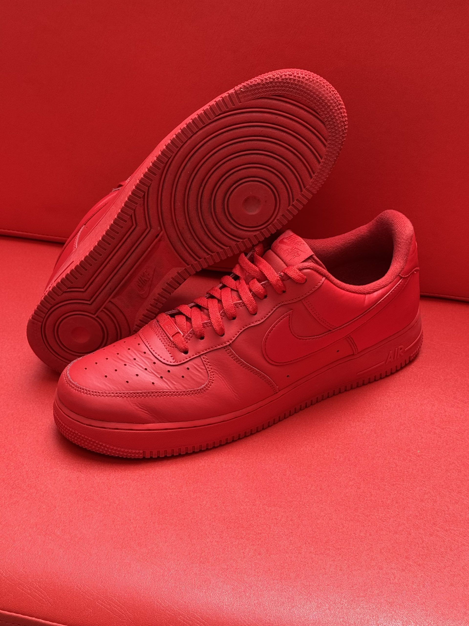 Red Nike Air Force 1 sneakers on a red surface, one sole up.