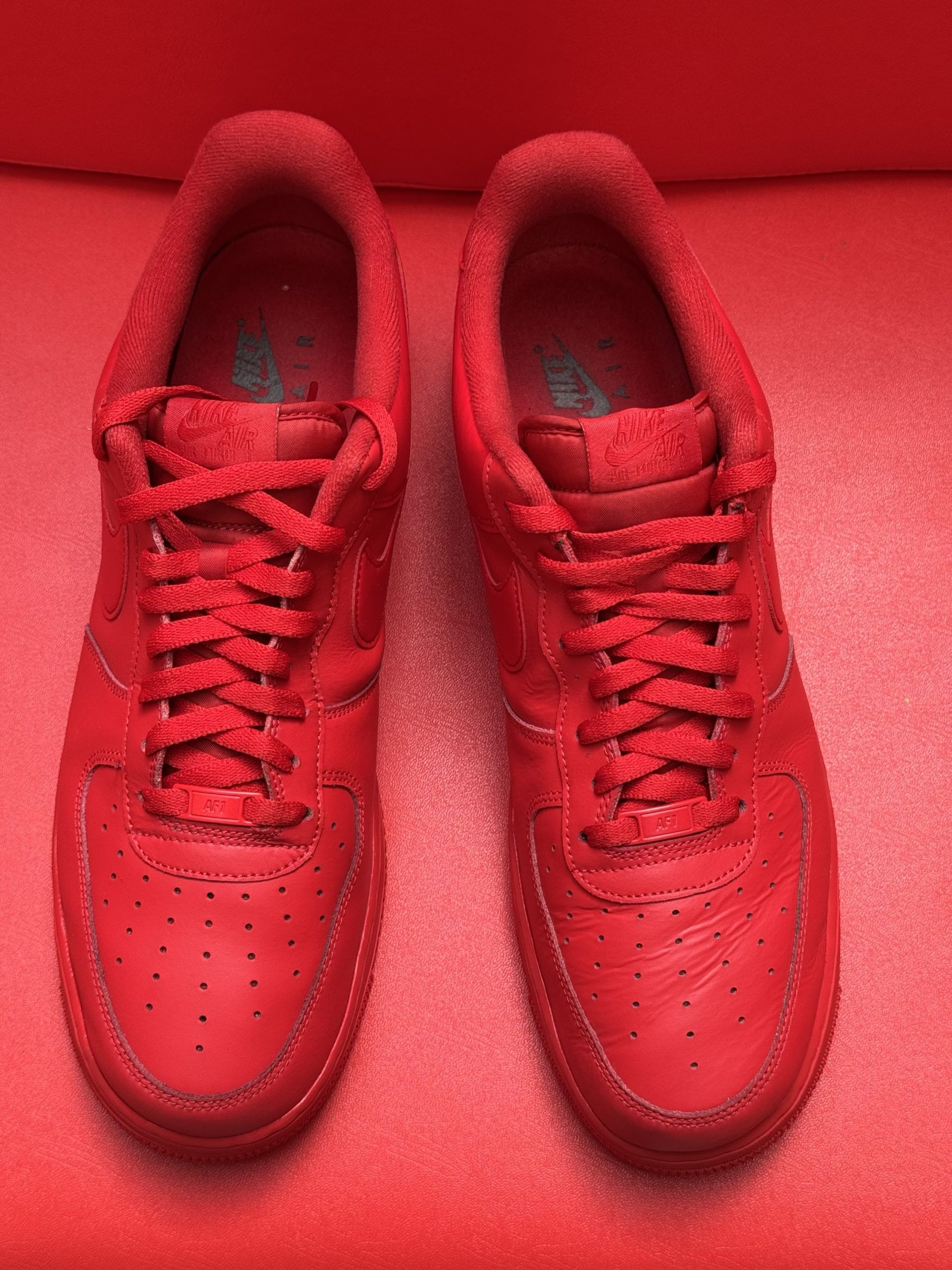 Red Nike Air Force 1 sneakers on a red surface, one sole up.
