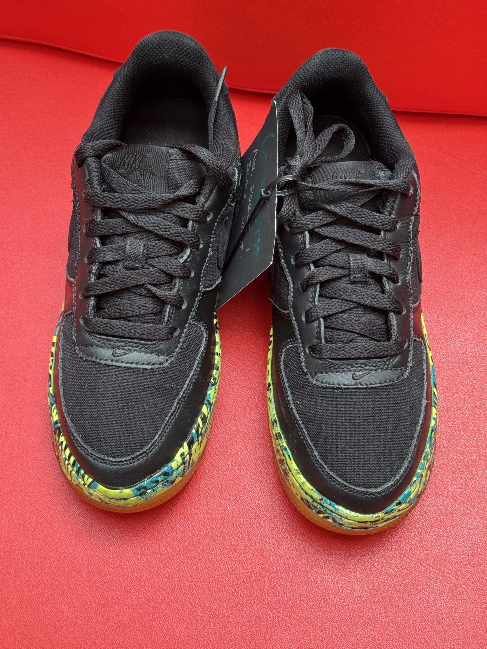 Black sneakers with patterned soles and laces, on a red surface.