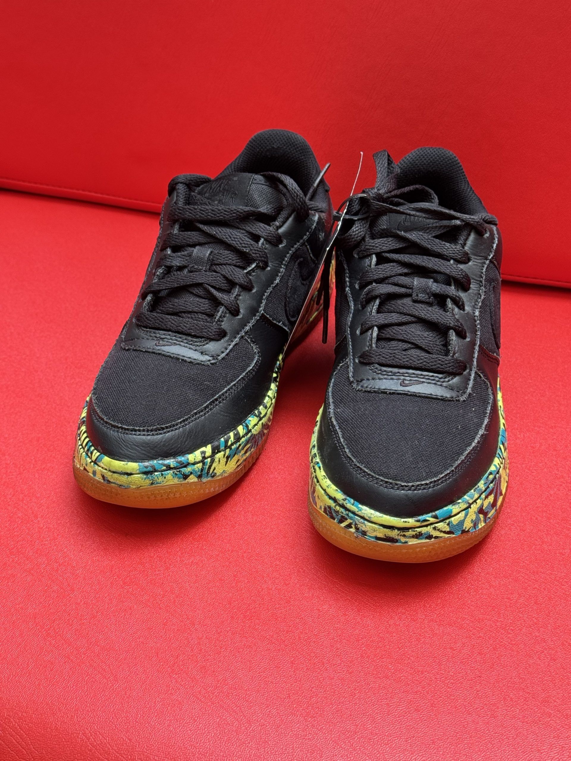 Black sneakers with patterned soles and laces, on a red surface.