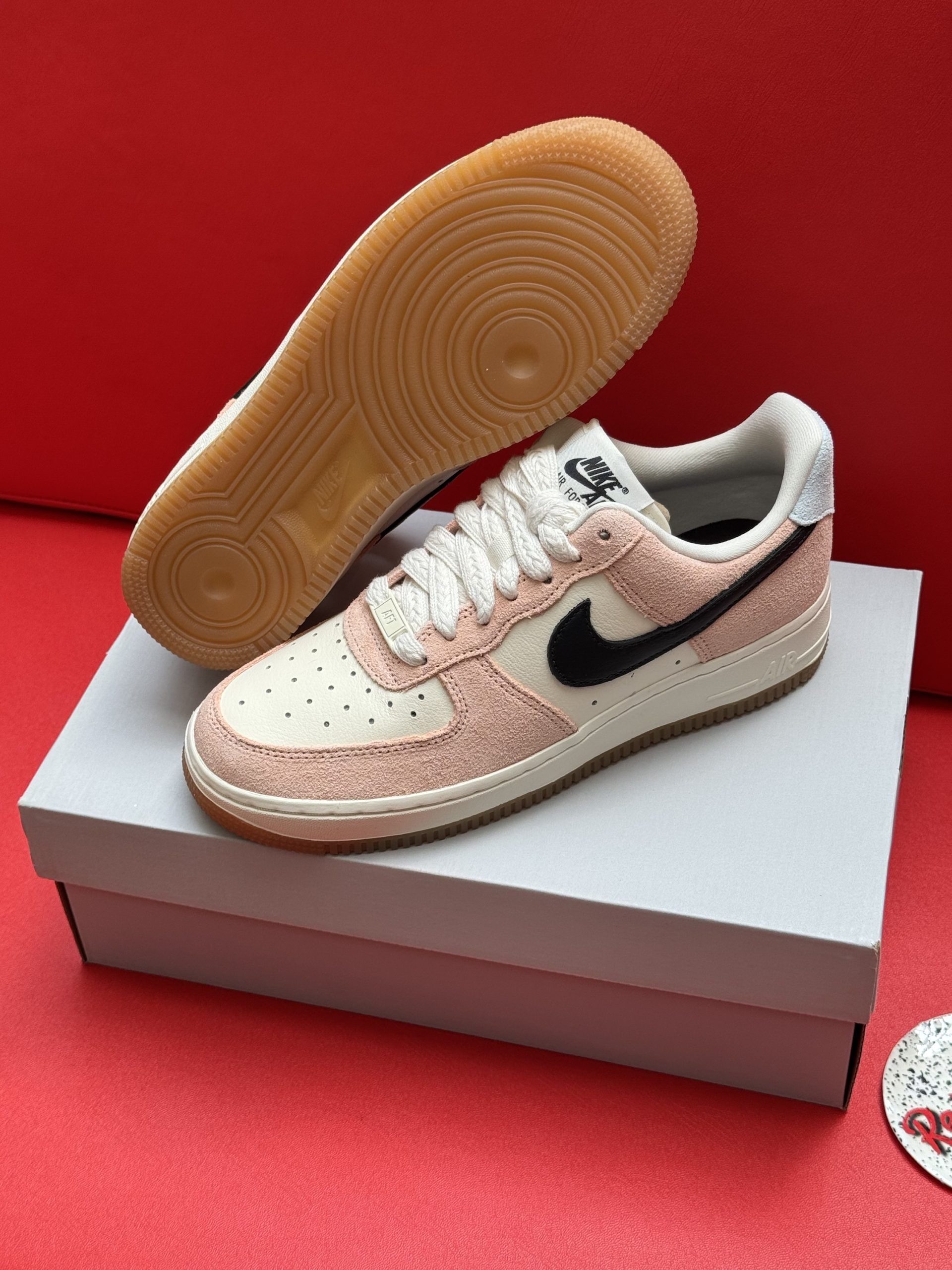 Pink and cream Nike Air Force 1 sneakers with black swoosh, sitting on white box, with the sole visible.