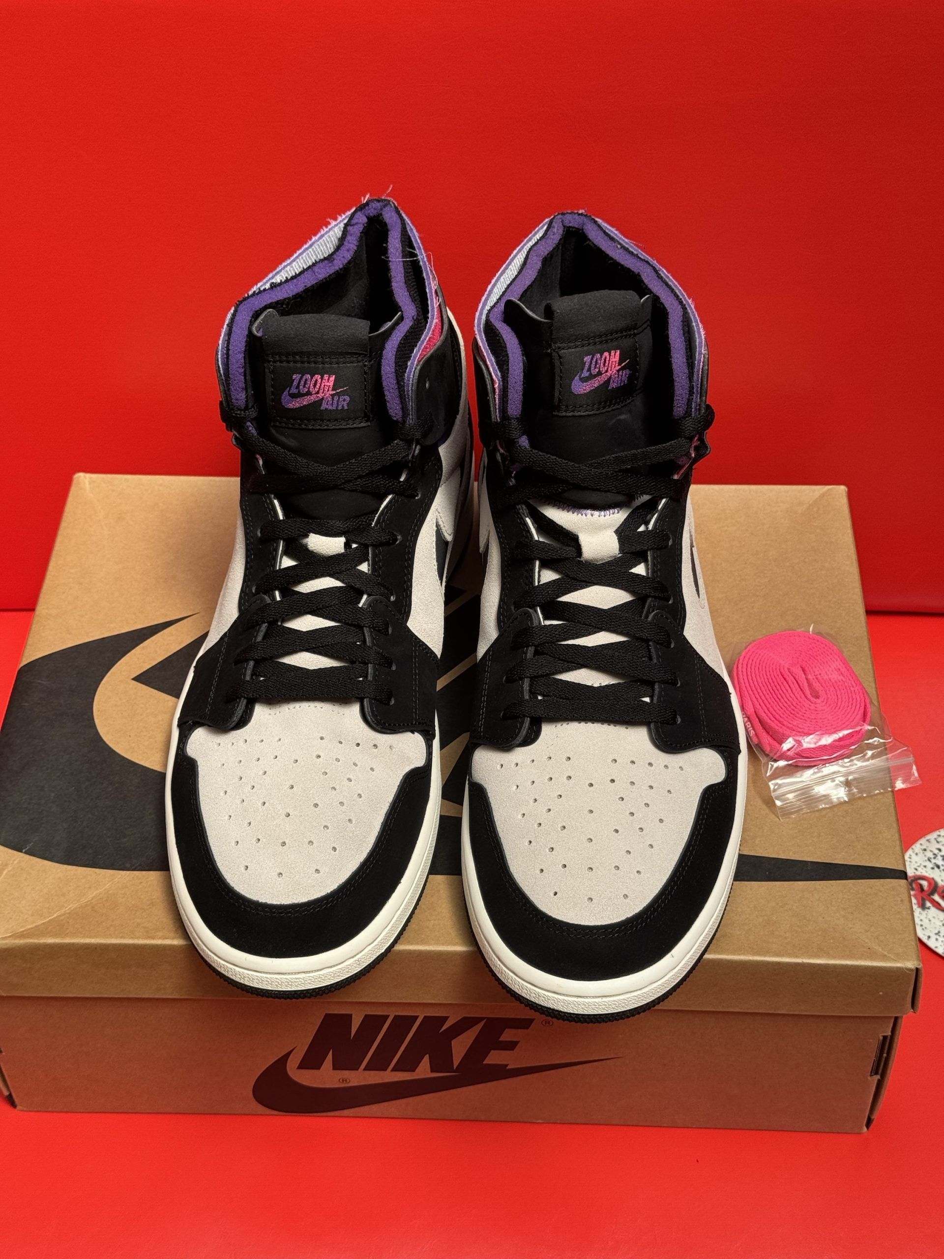 Air Jordan 1 sneakers on shoebox, purple sole, with extra laces and pink accessories.