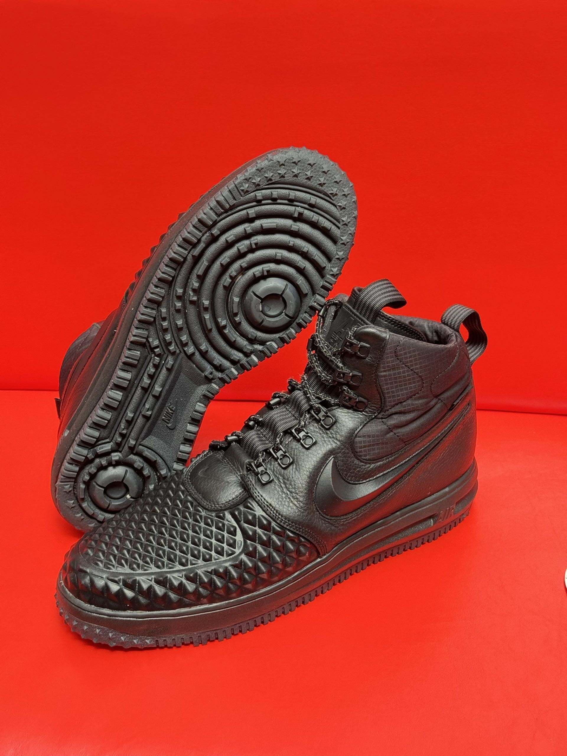 Black Nike high-top sneakers with textured uppers, laces, and tread, on a red surface.