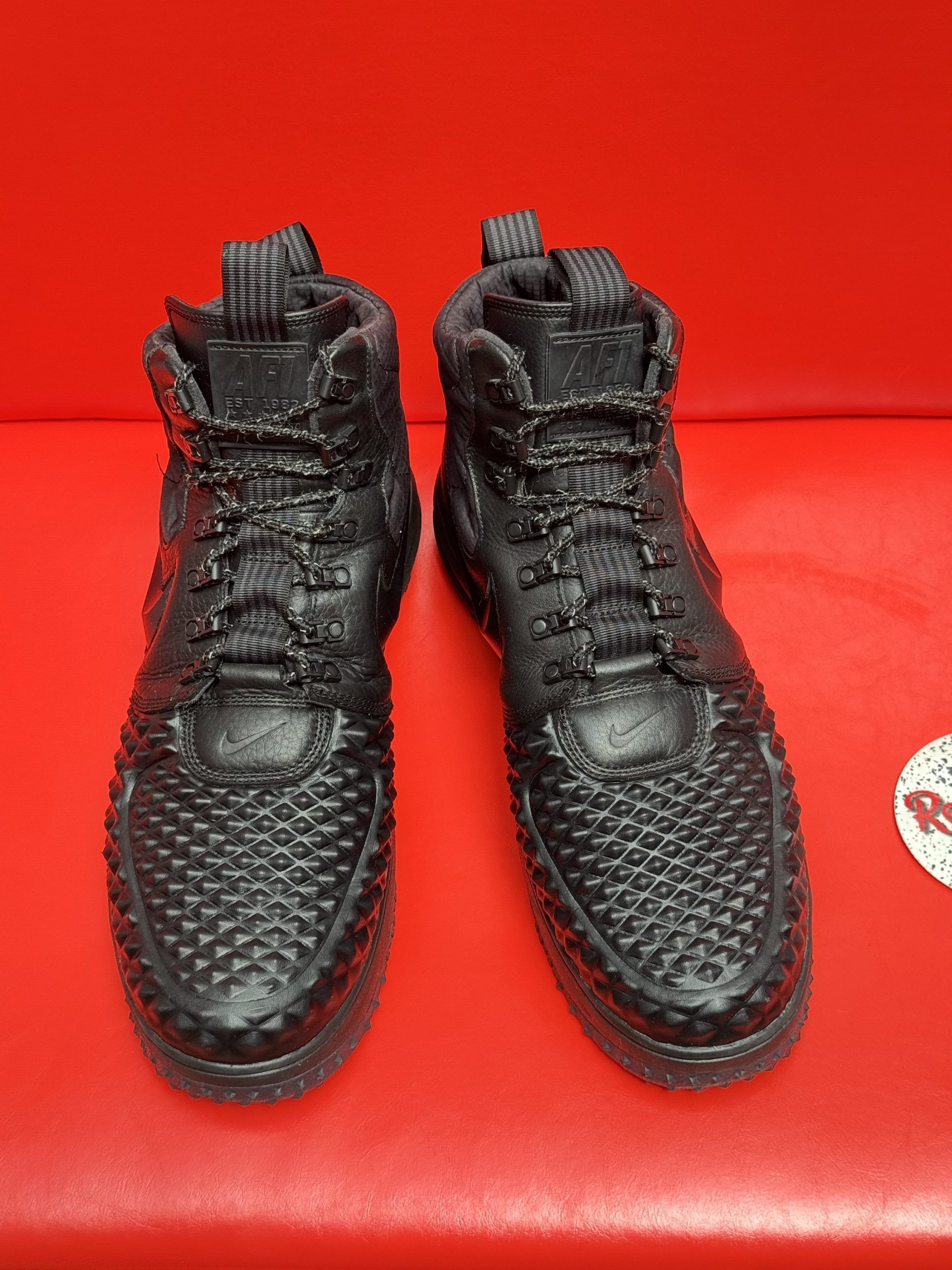 Black Nike high-top sneakers with textured uppers, laces, and tread, on a red surface.