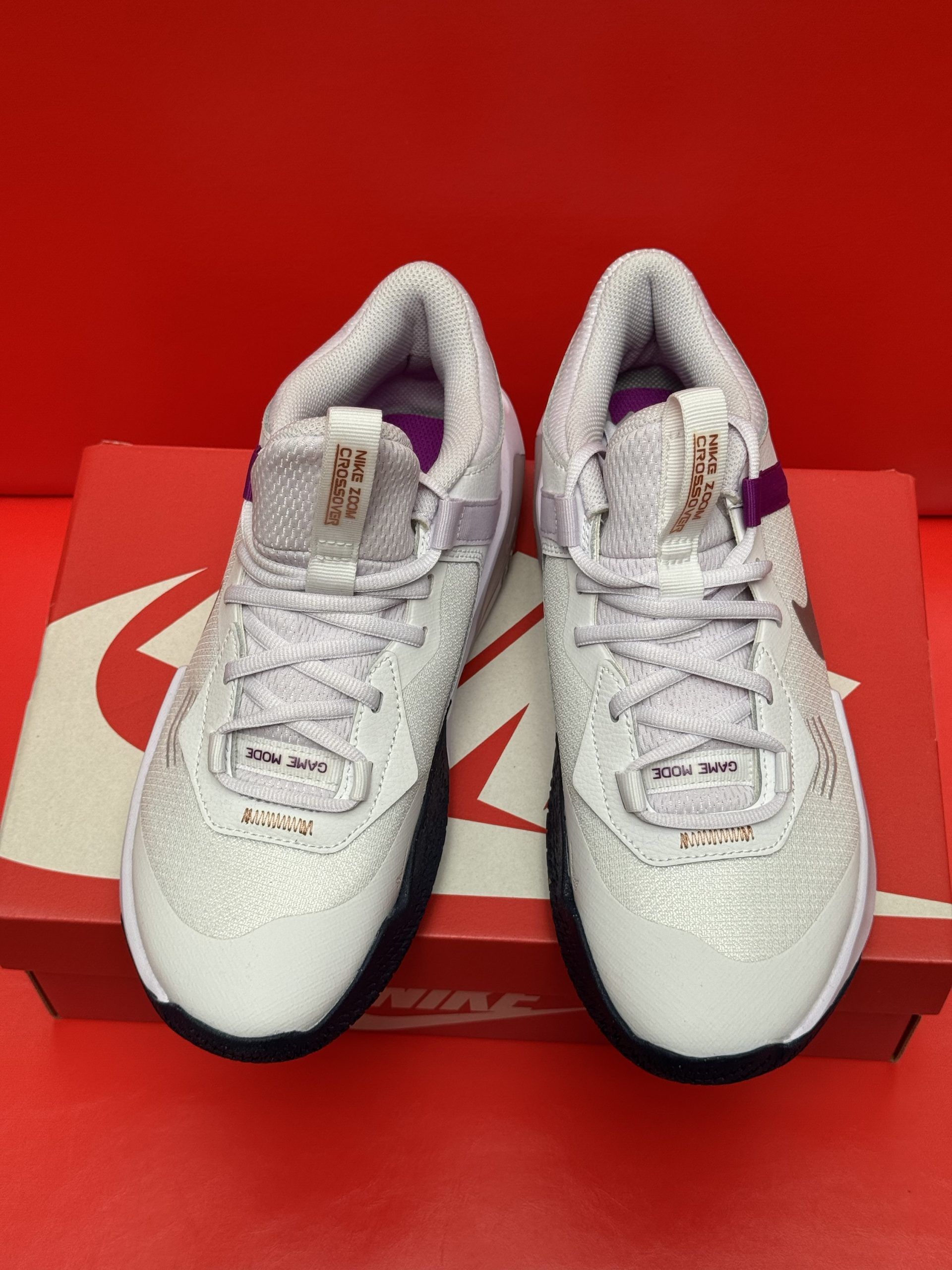 White Nike basketball sneakers with purple accents, on a Nike box, set against a red background.