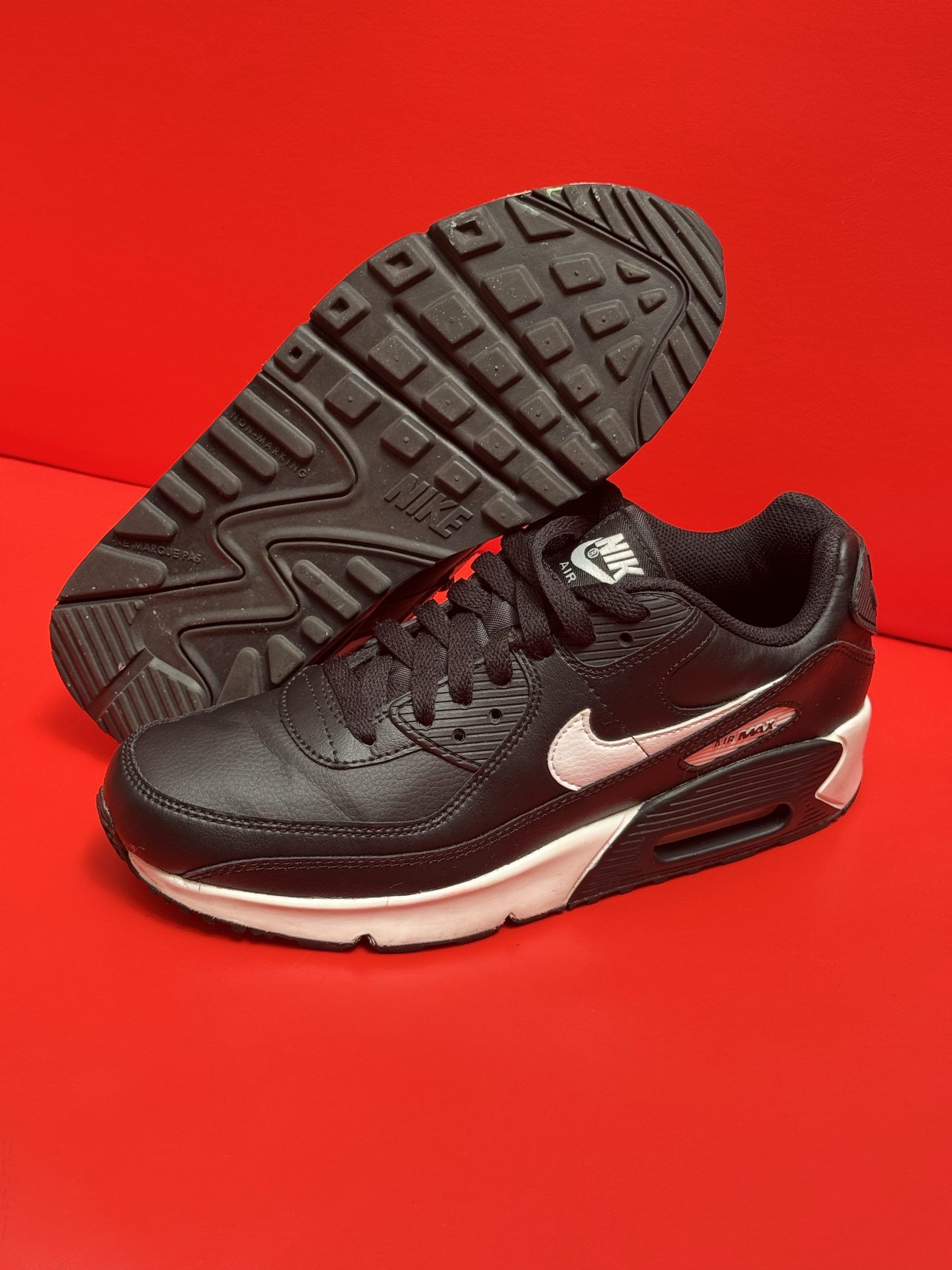 Black Nike Air Max 90 sneakers with white accents and sole, on a red surface.