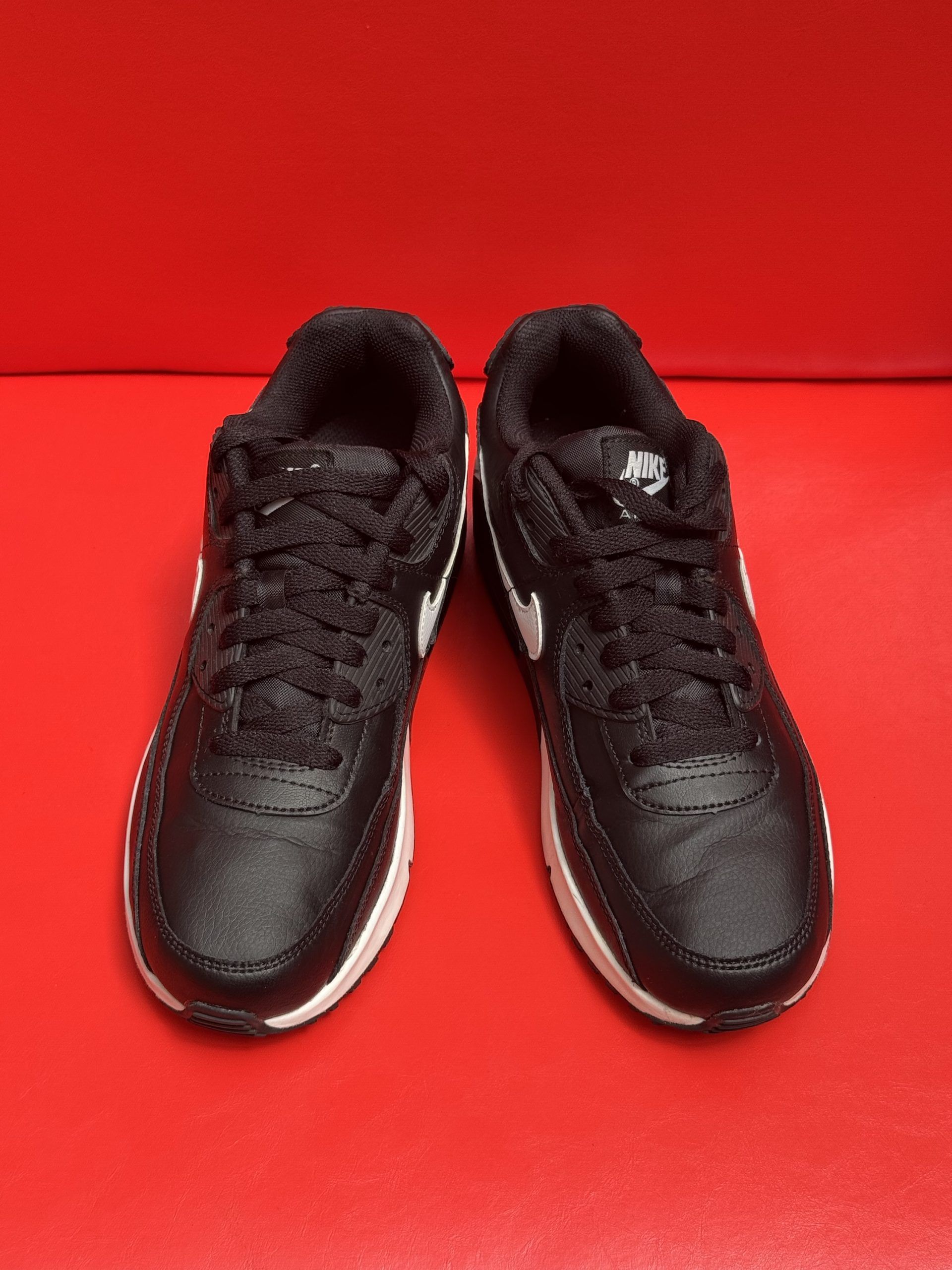 Black Nike Air Max 90 sneakers with white accents and sole, on a red surface.