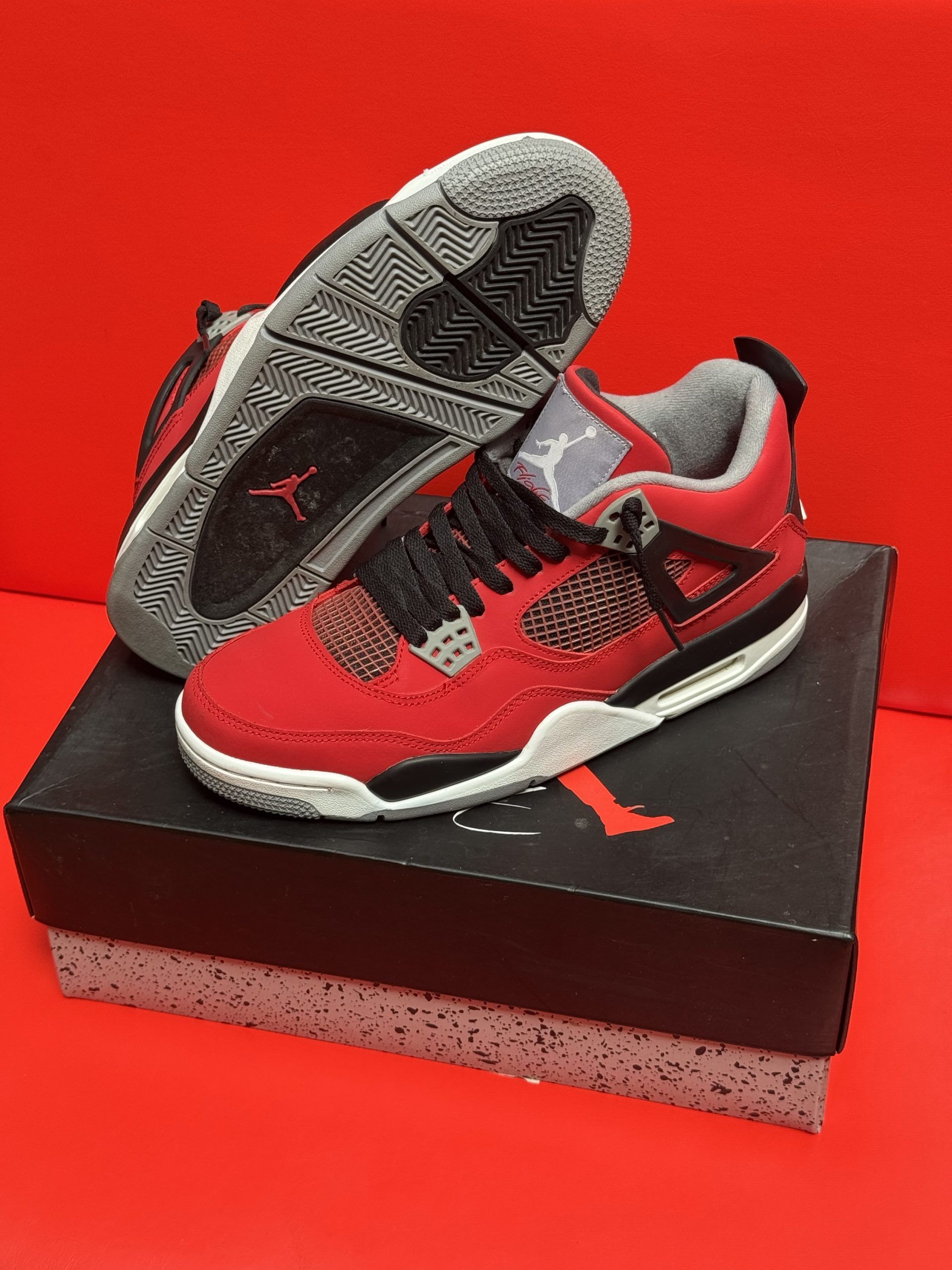 Red and black Air Jordan 4 sneakers on top of a black and gray shoe box with a red background.