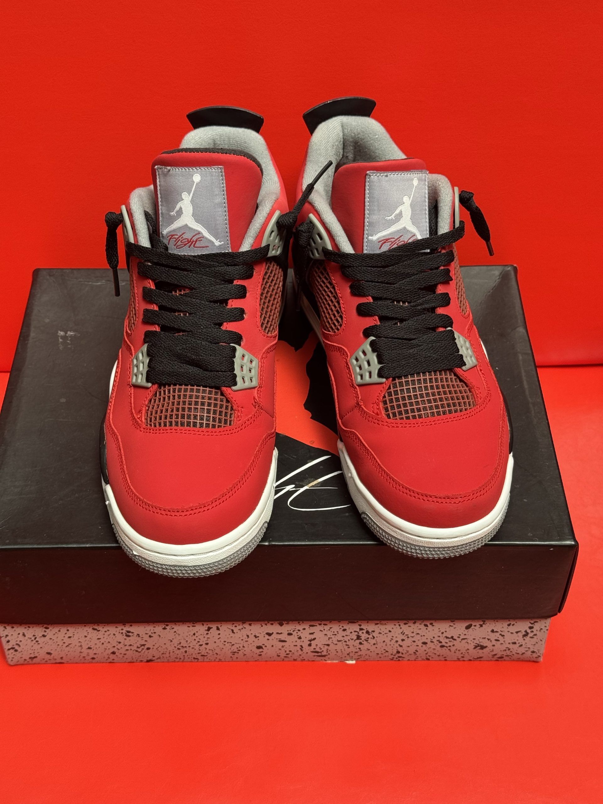Red and black Air Jordan 4 sneakers on top of a black and gray shoe box with a red background.