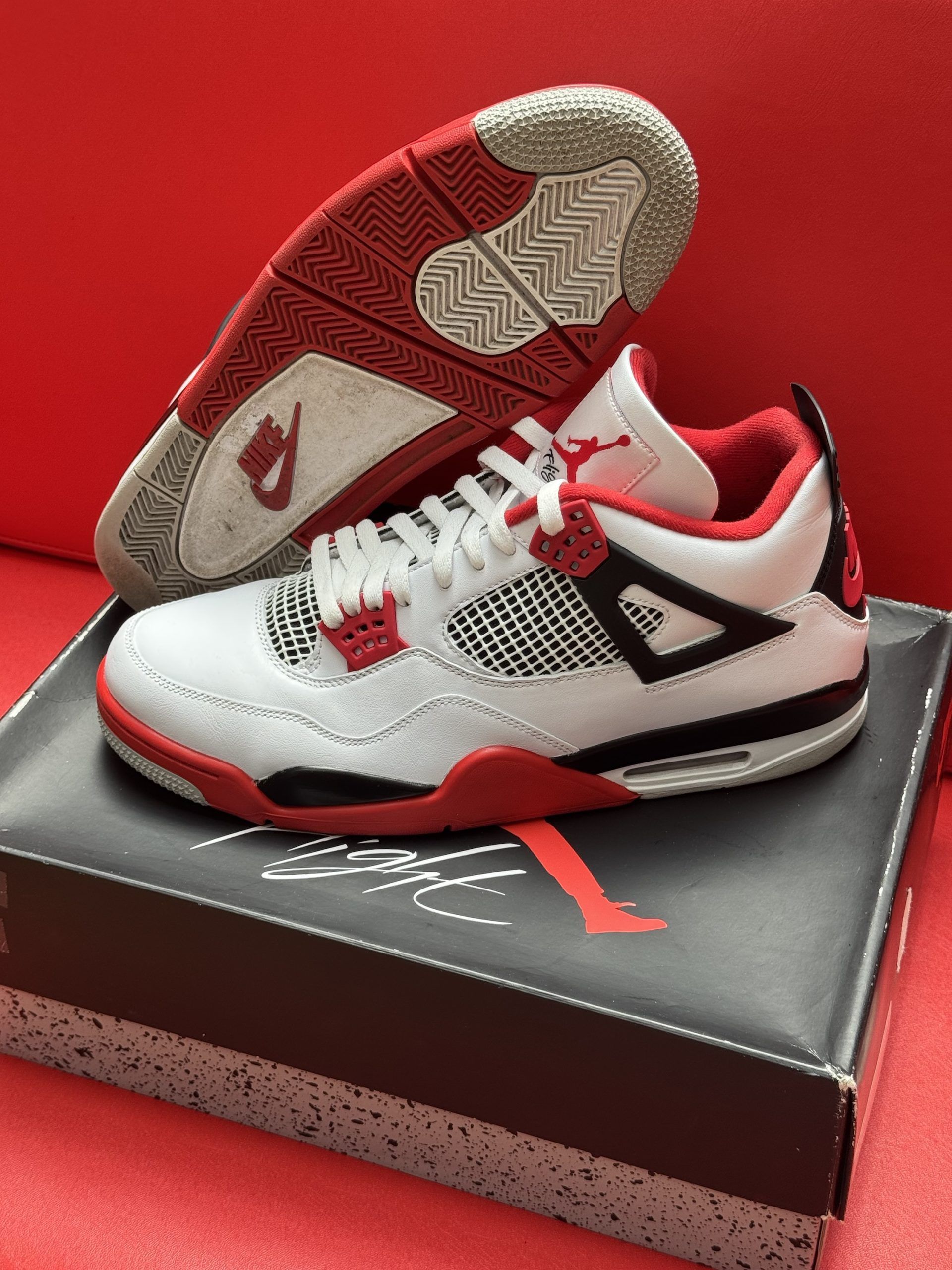 White, red, and black Air Jordan 4 sneakers on top of the shoe box, red sole visible.