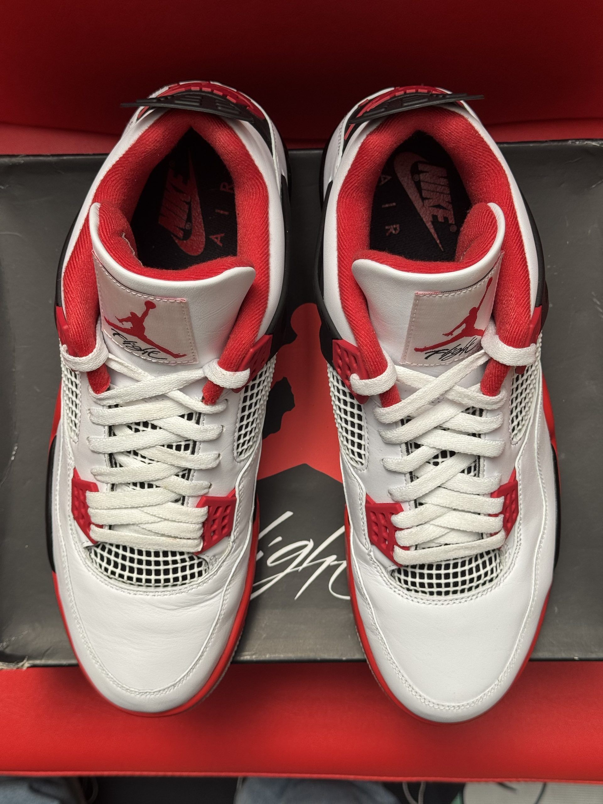 White, red, and black Air Jordan 4 sneakers on top of the shoe box, red sole visible.