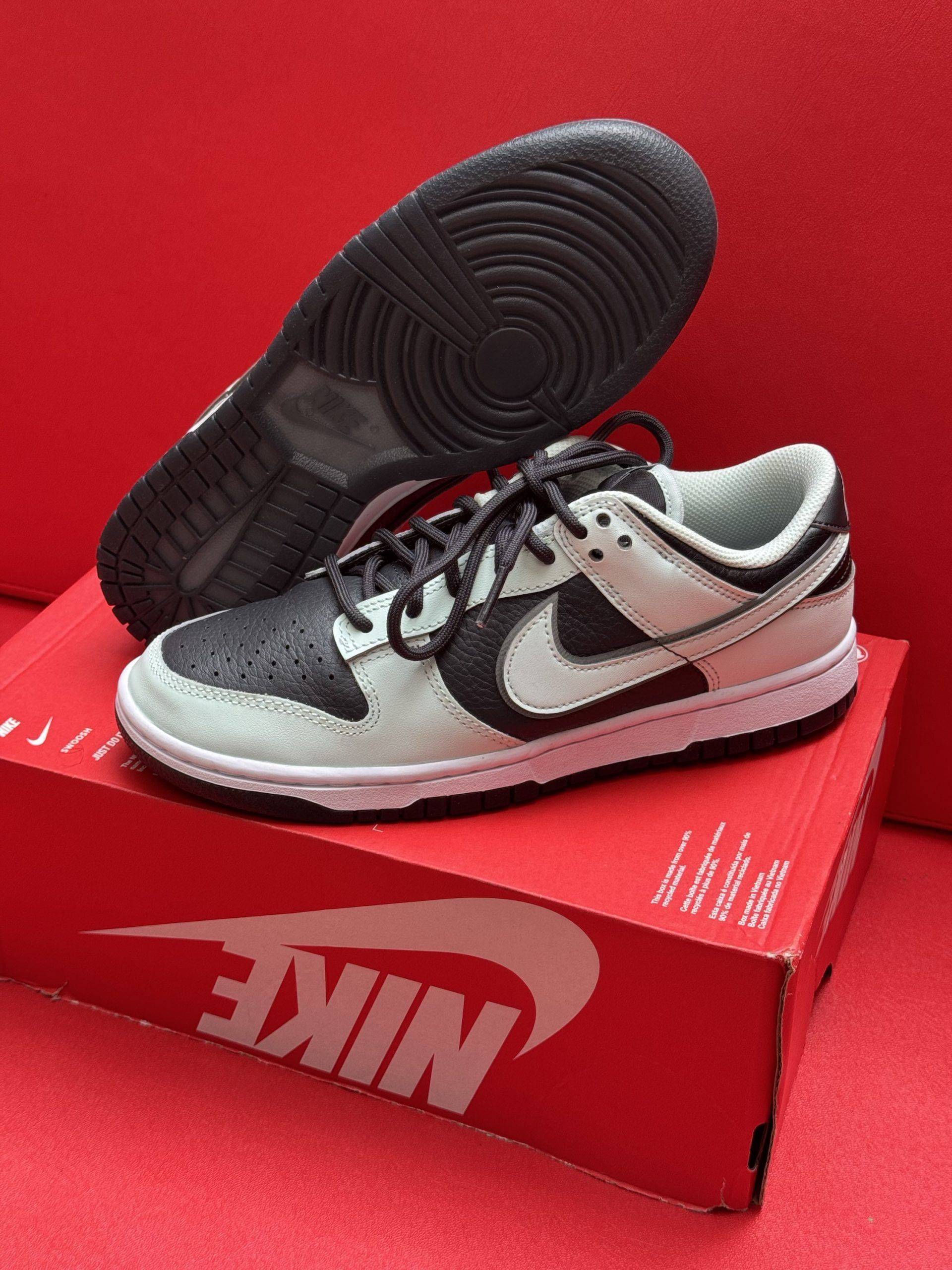 Pair of black and light grey Nike Dunk Low sneakers on a red Nike box with a black sole.