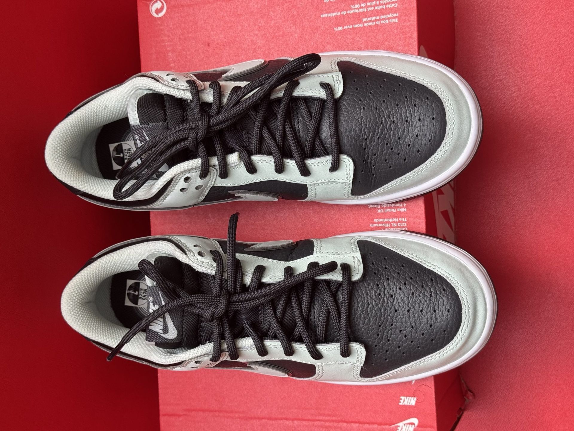 Pair of black and light grey Nike Dunk Low sneakers on a red Nike box with a black sole.