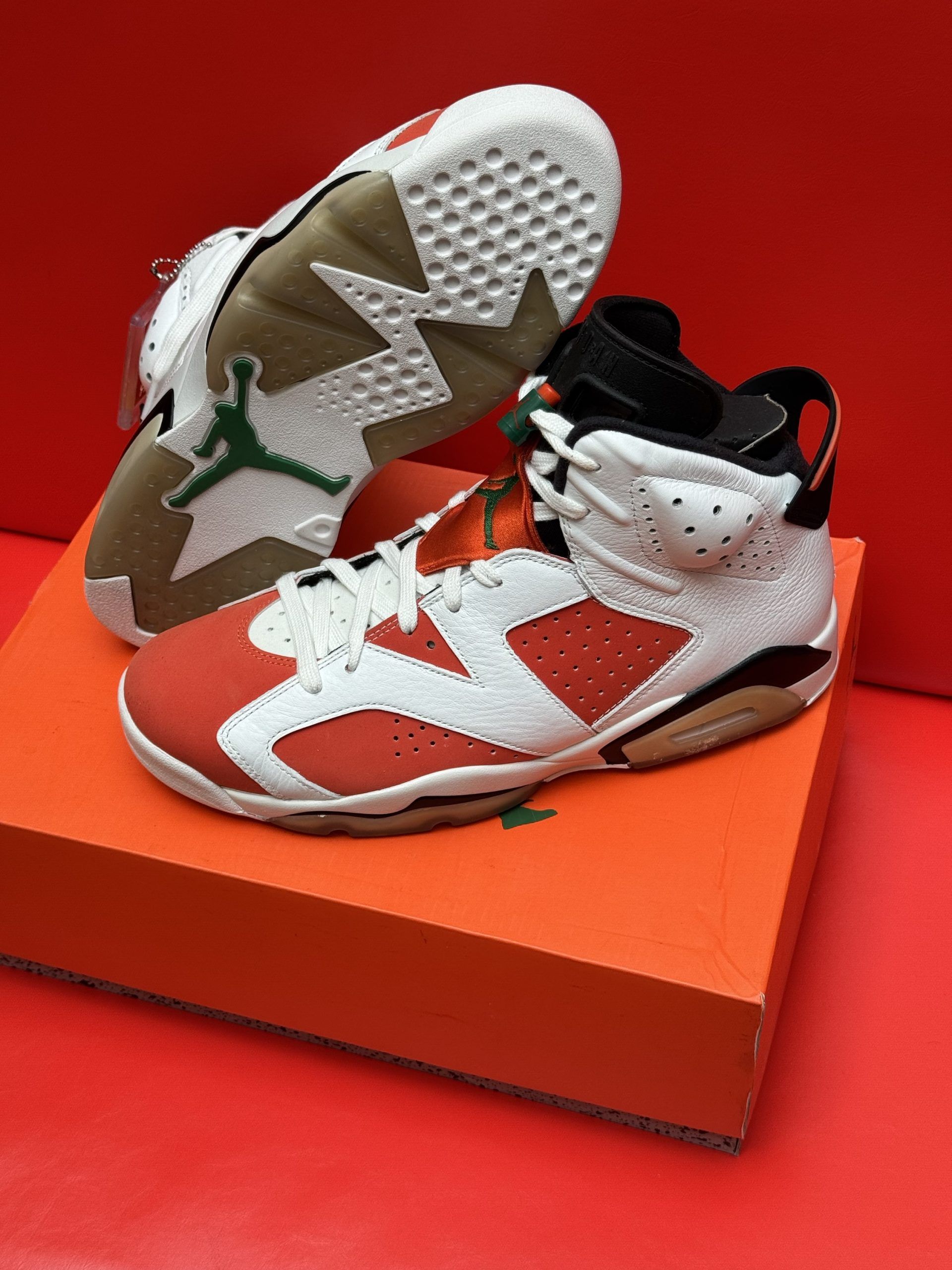 Air Jordan 6 sneakers in white and orange on an orange box, red background.