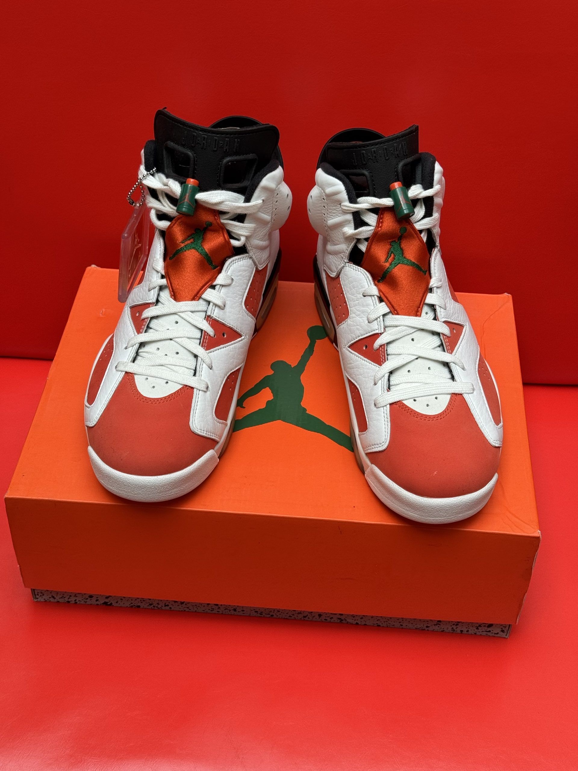 Air Jordan 6 sneakers in white and orange on an orange box, red background.