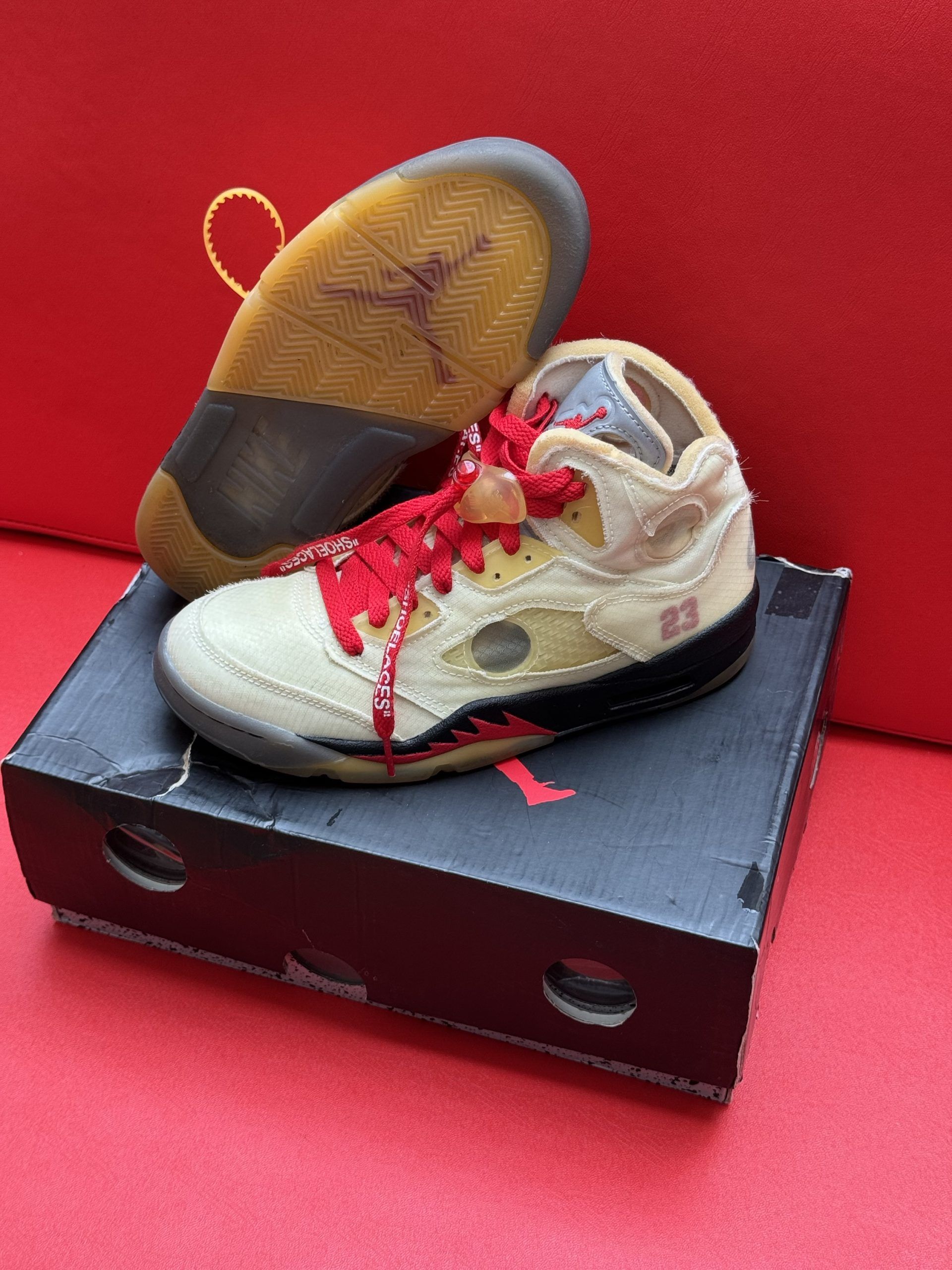 Air Jordan 5 Off-White sneakers on top of their box, with one sole visible, all on a red surface.
