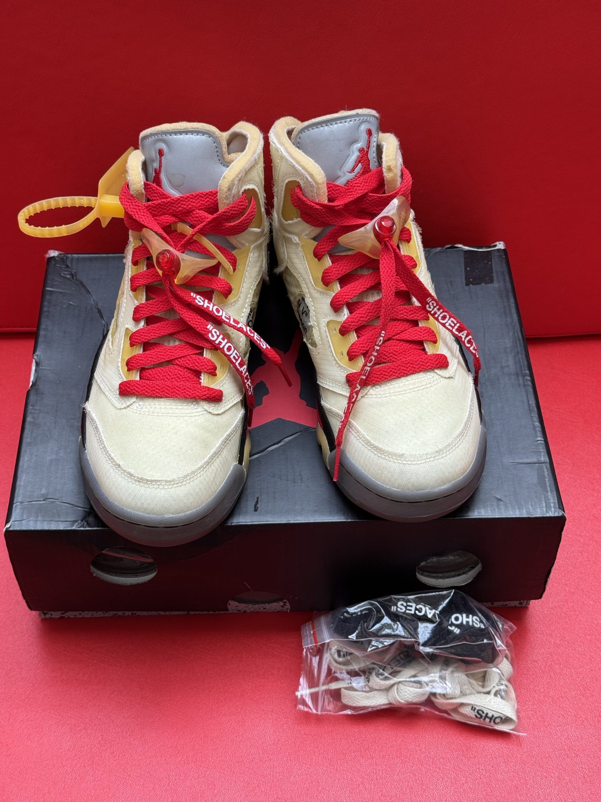 Air Jordan 5 Off-White sneakers on top of their box, with one sole visible, all on a red surface.