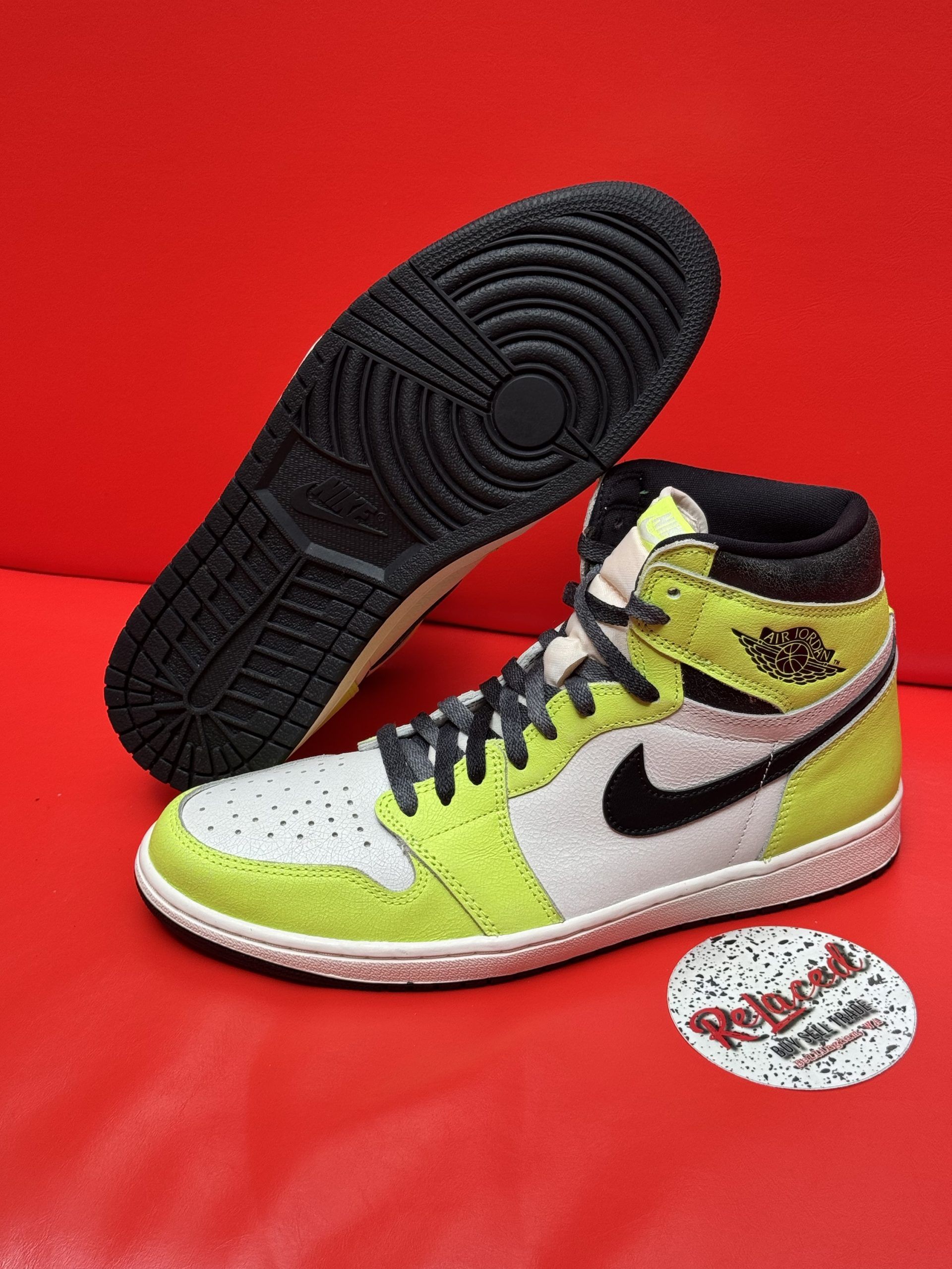 Air Jordan 1 high-top sneaker, white and neon yellow panels, black swoosh, black sole, on red surface.