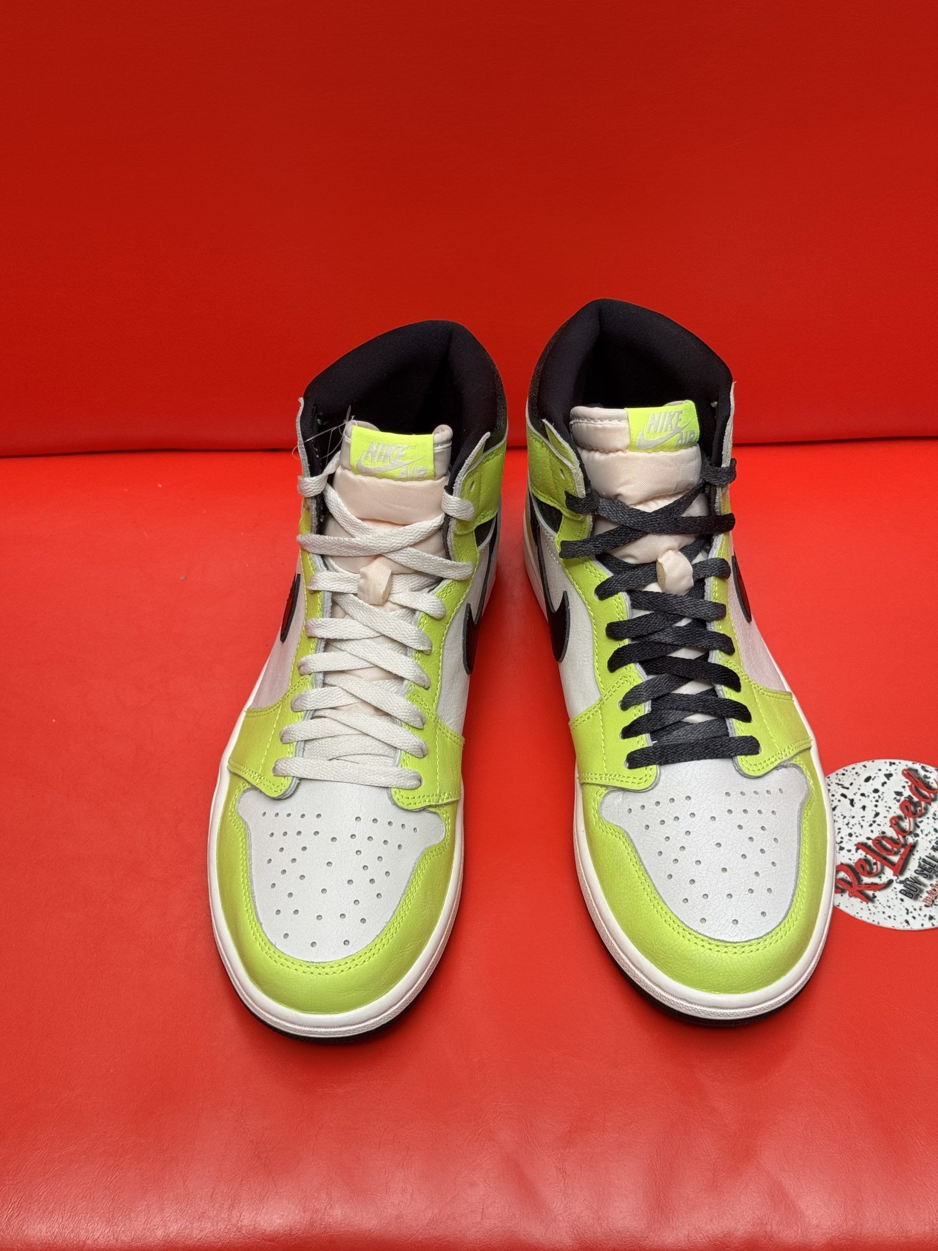 Air Jordan 1 high-top sneaker, white and neon yellow panels, black swoosh, black sole, on red surface.