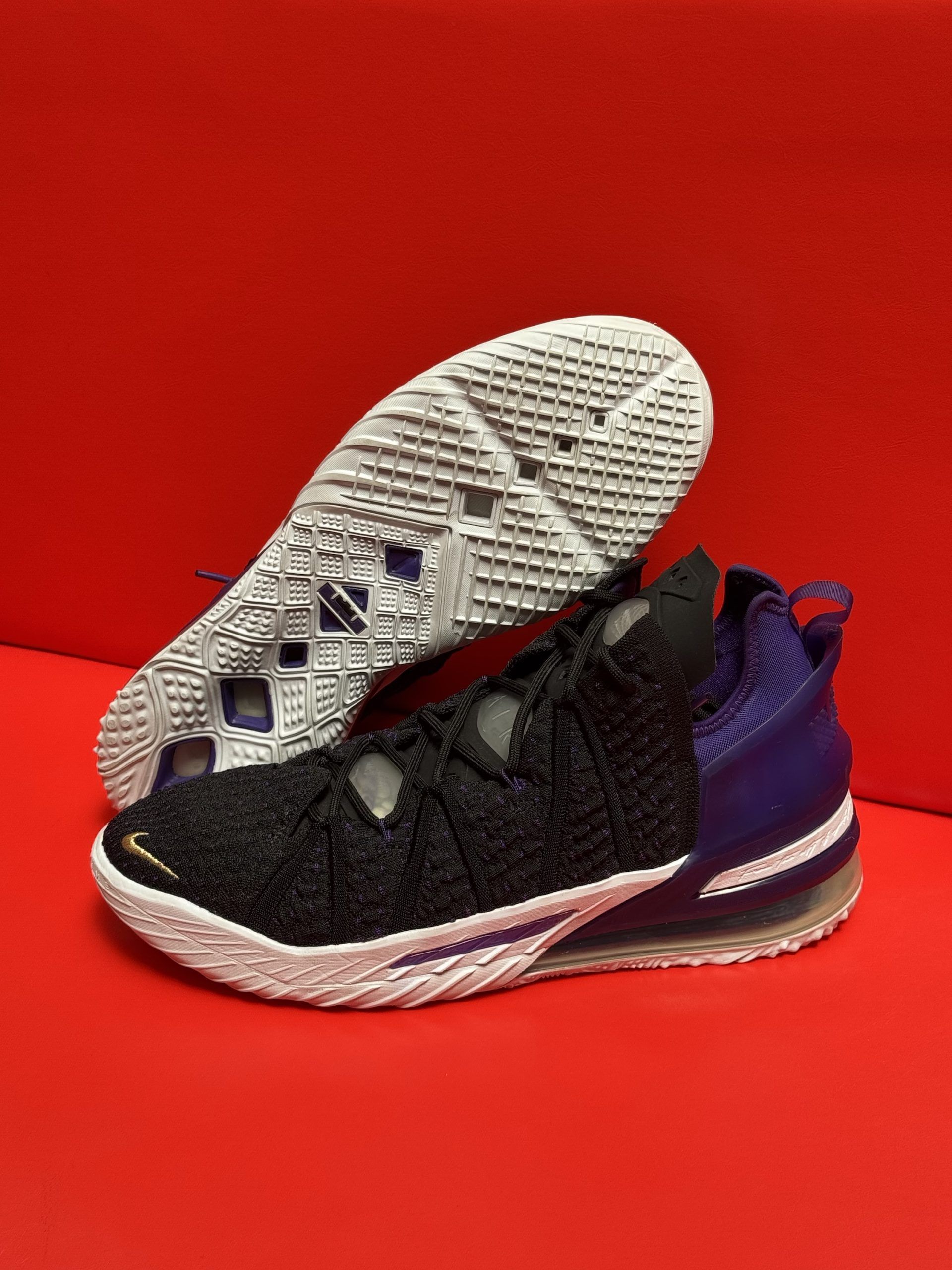 Black and purple Nike LeBron 18 basketball sneakers with white soles, set against a red background.